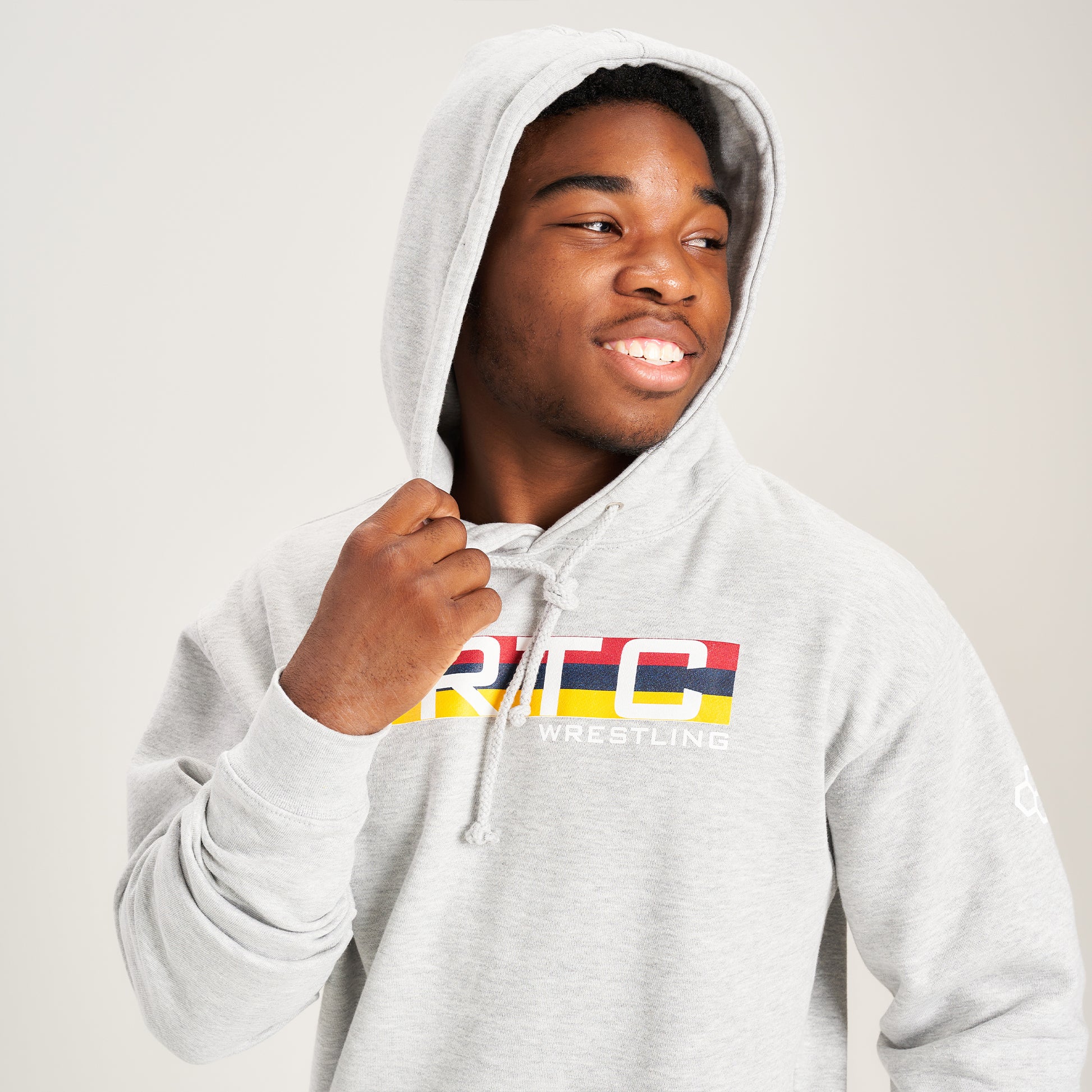 This image features a young man wearing a gray hoodie with the text RTC WRESTLING prominently displayed smiling while pulling the hood close to his head