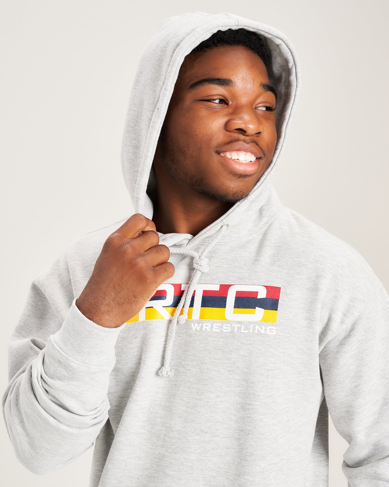 A young man wearing a light gray hoodie featuring a colorful logo that reads RTC WRESTLING exuding a friendly and confident demeanor while facing slightly to the side