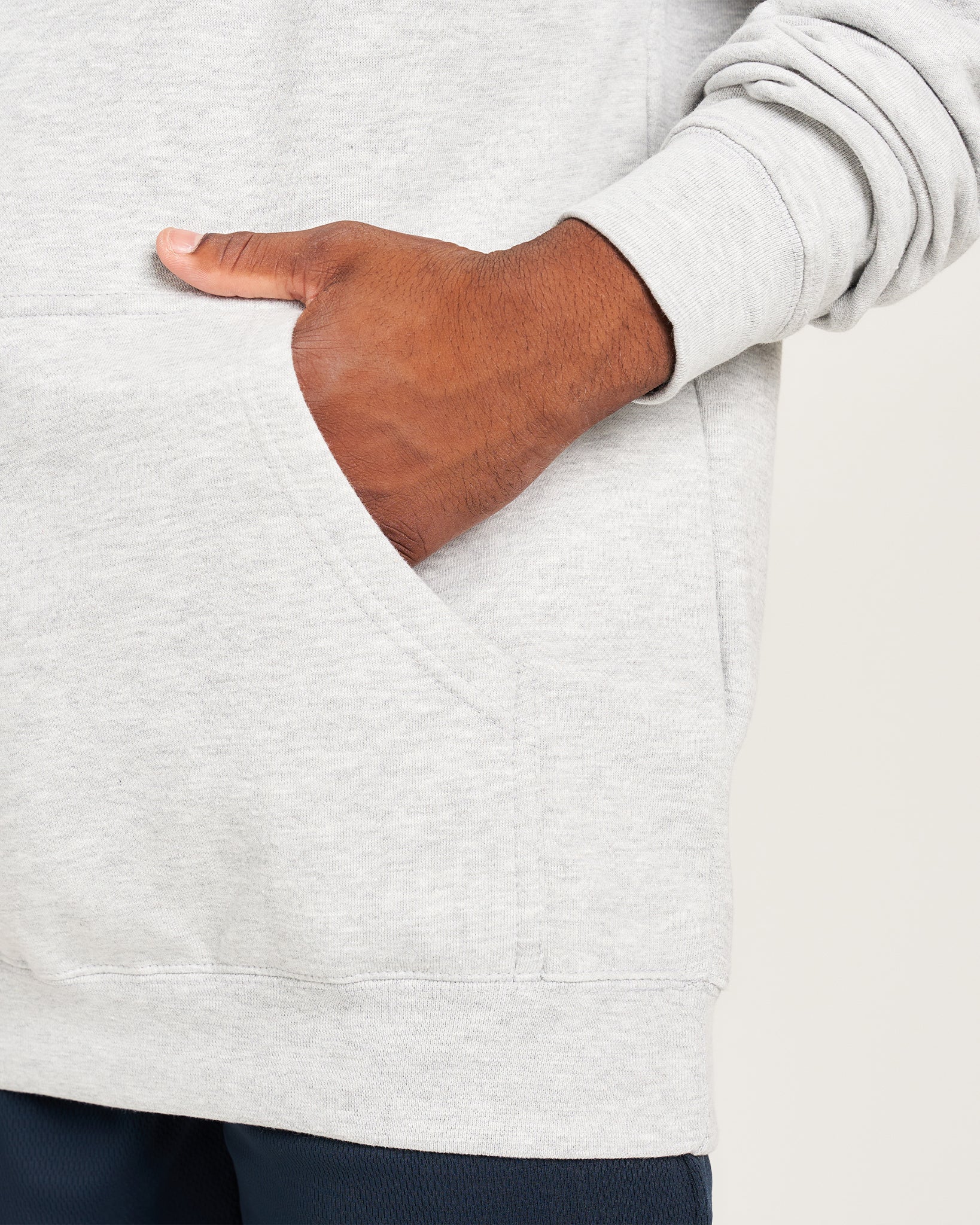 A close-up view of a person wearing a light gray hoodie with one hand in the pocket highlighting the fabric texture and casual style