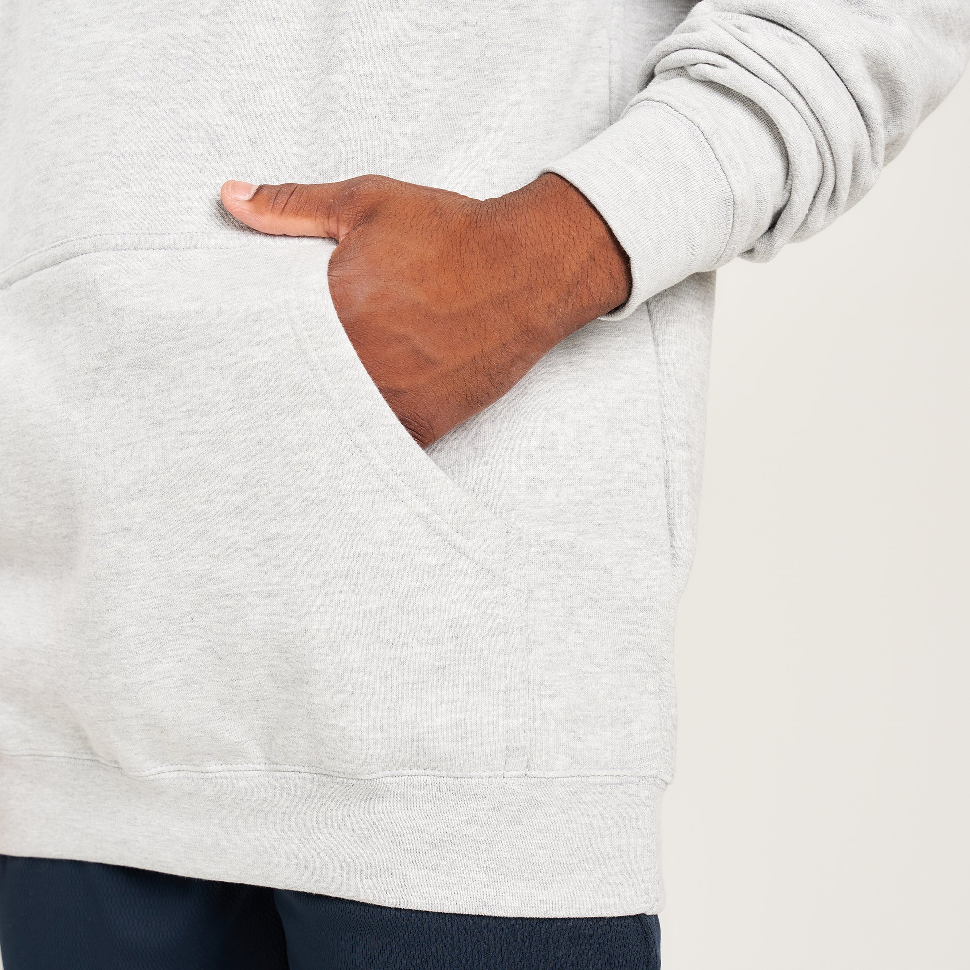 A close-up of a person wearing a light gray hoodie with a visible front pocket showcasing a hand resting in the pocket