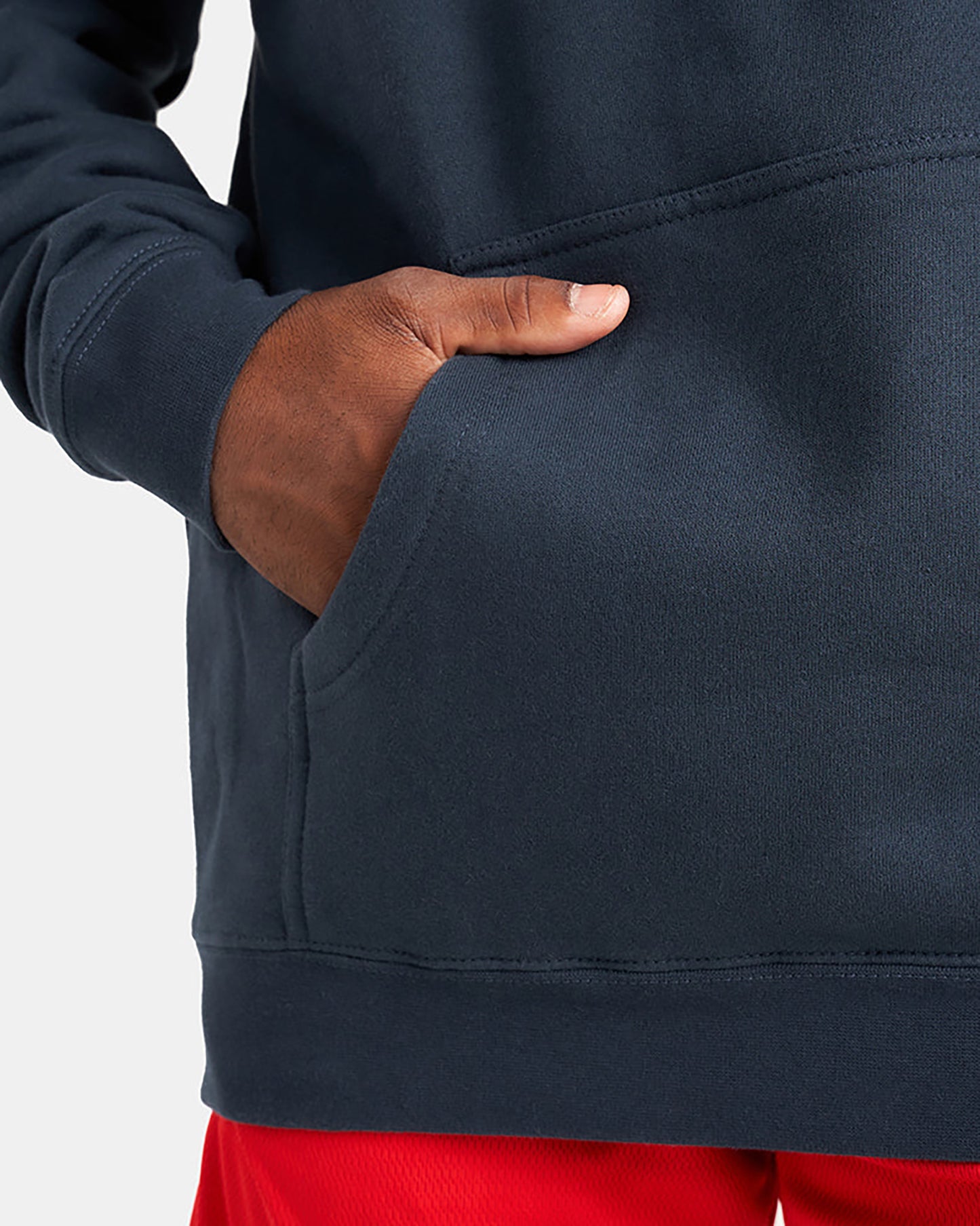 A close-up view of a hand placed in the pocket of a dark navy sweatshirt paired with bright red shorts