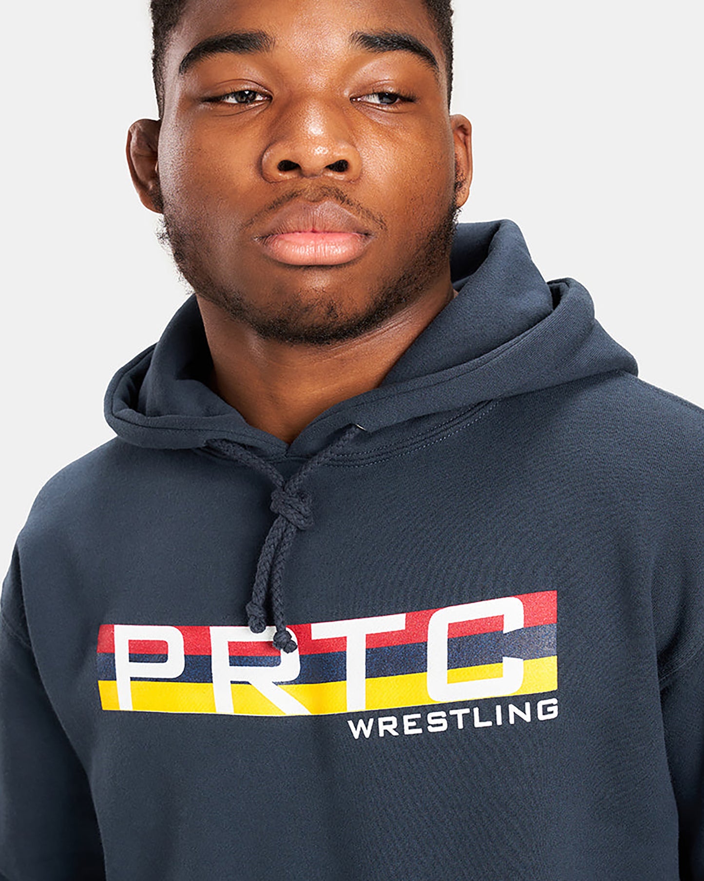 A young man wearing a dark blue hoodie featuring a colorful PRTC WRESTLING graphic design