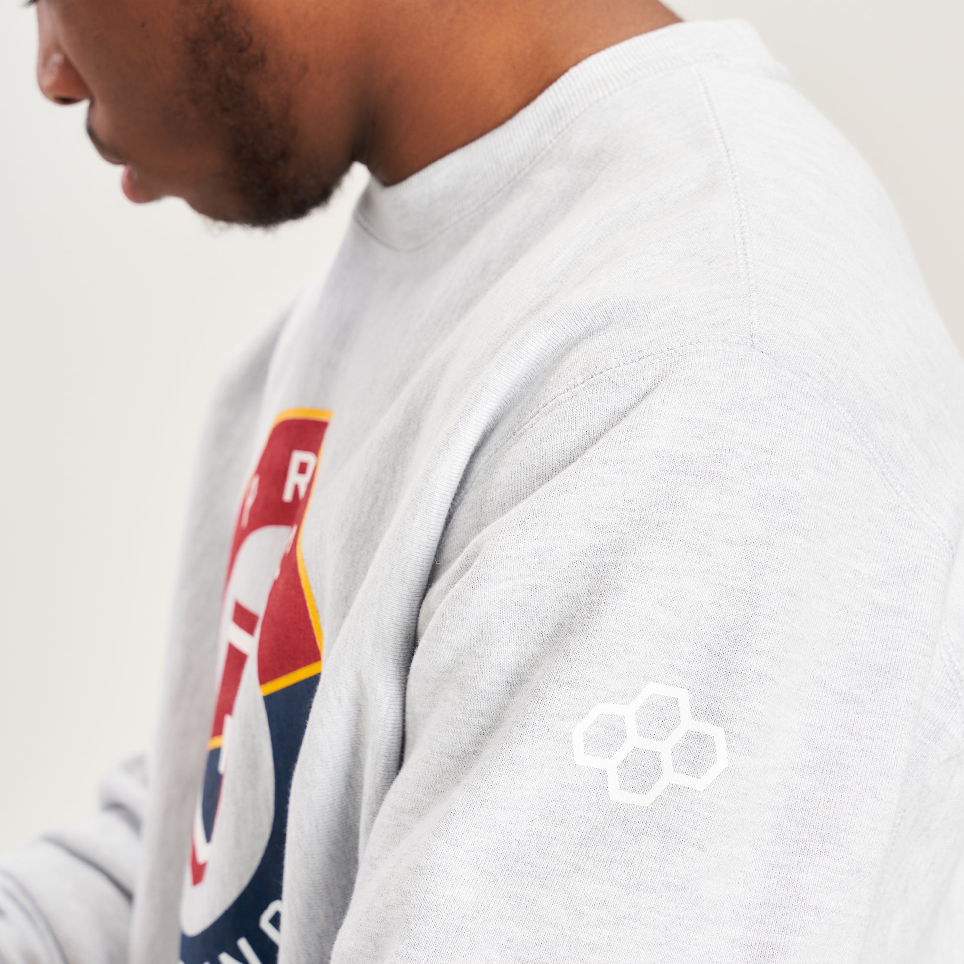 A profile view of a person wearing a light gray sweatshirt featuring a colorful logo on the front and a distinct design element on the sleeve