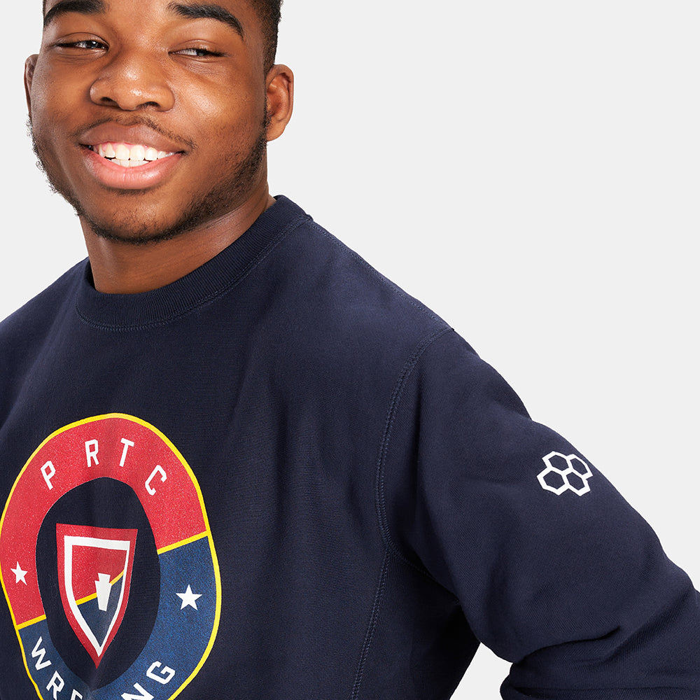 A young man smiles while wearing a navy sweatshirt with a vibrant graphic design related to wrestling