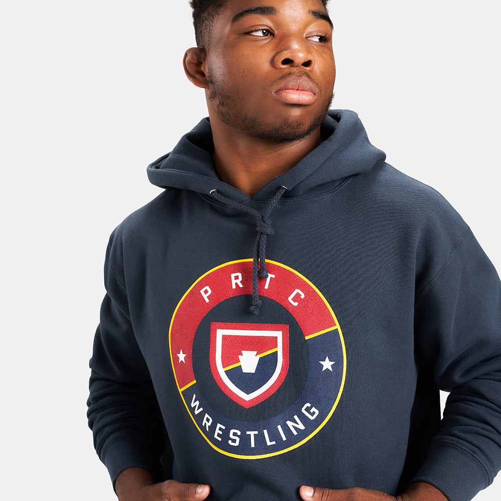 A young man wearing a dark hoodie featuring a circular wrestling logo with bold colors and text