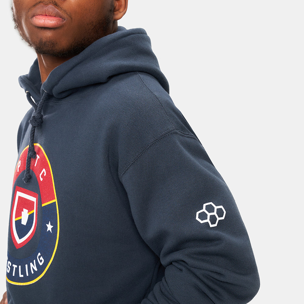 A close-up profile of a young man wearing a navy blue hoodie featuring a colorful wrestling logo on the chest and a distinctive graphic on the sleeve