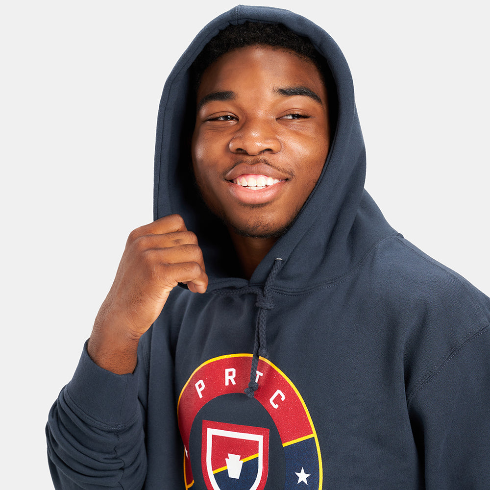 A young man wearing a navy-blue hoodie with a graphic logo smiles warmly showcasing a casual and confident demeanor