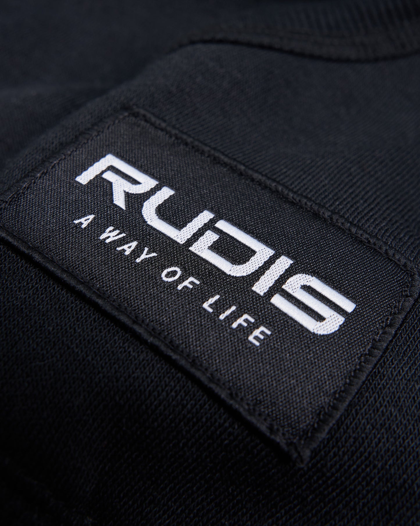 A close-up of a black fabric label featuring the RUDIS A WAY OF LIFE logo emphasizing the brands identity and design