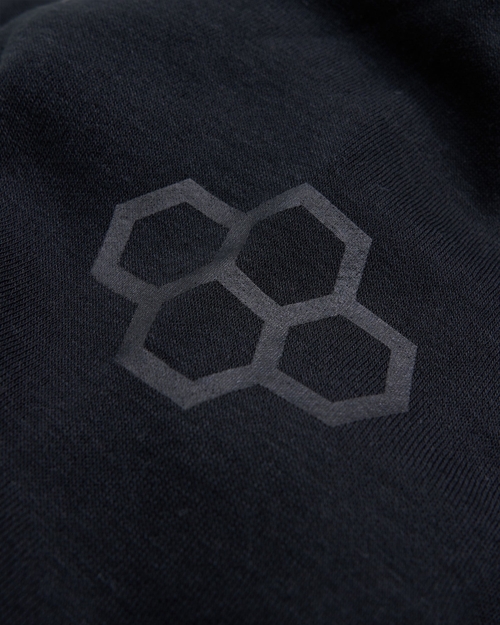 A close-up view of a dark fabric displaying a subtle logo composed of interlocking hexagons emphasizing a modern design aesthetic