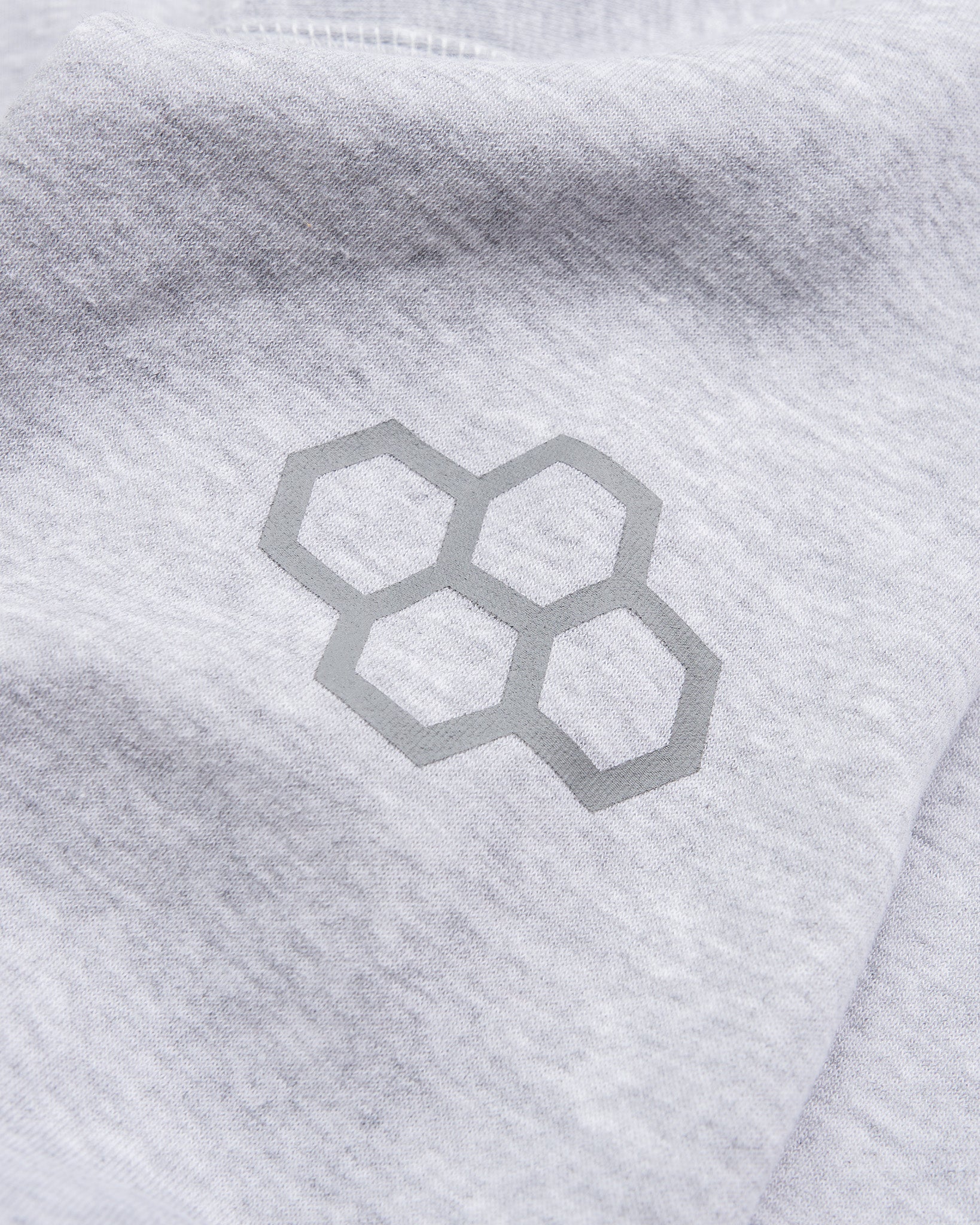 A close-up of a light gray fabric featuring a subtle hexagonal logo design in darker gray