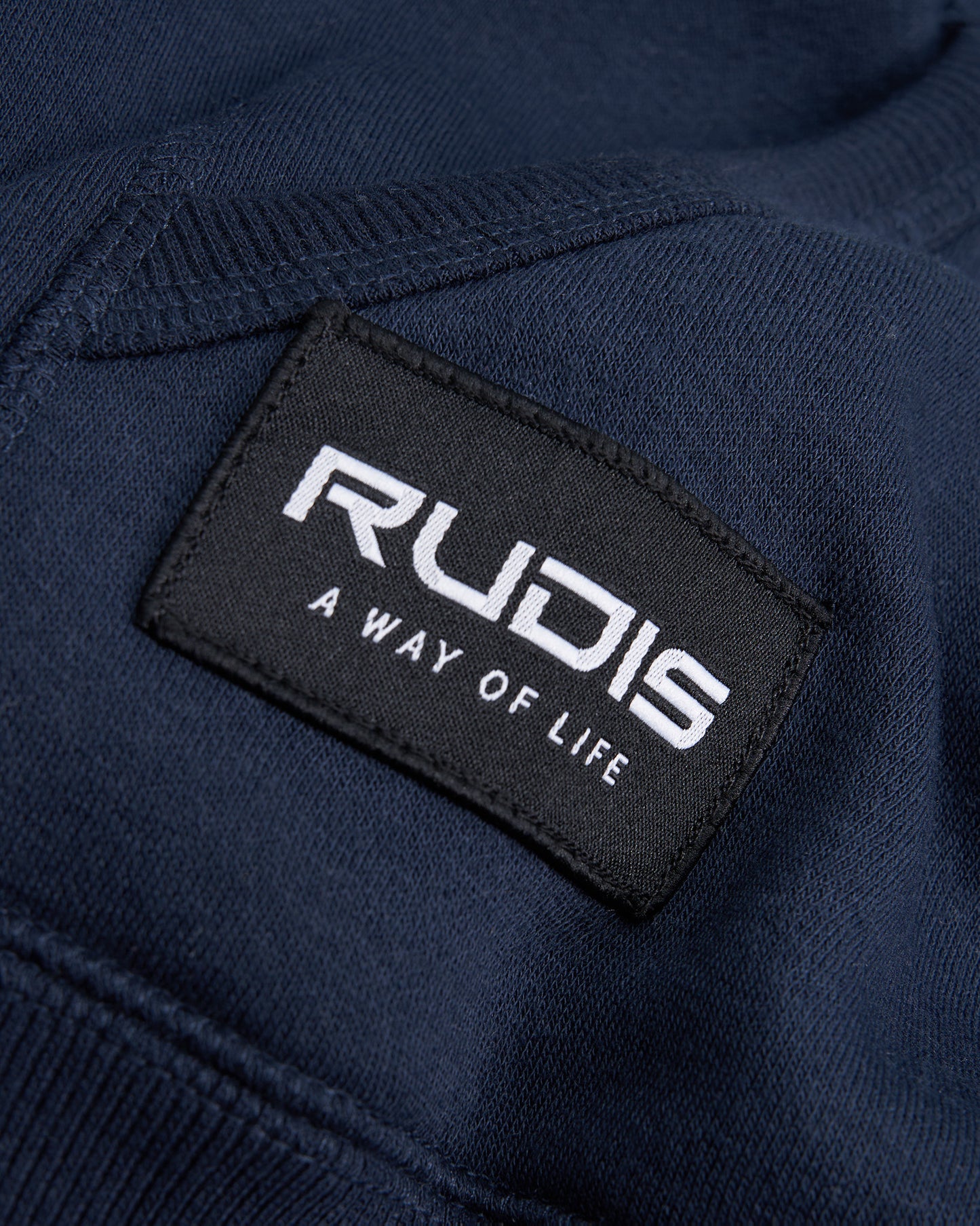 Close-up of a navy blue fabric featuring a prominent black label with the brand name RUDIS and the phrase A WAY OF LIFE