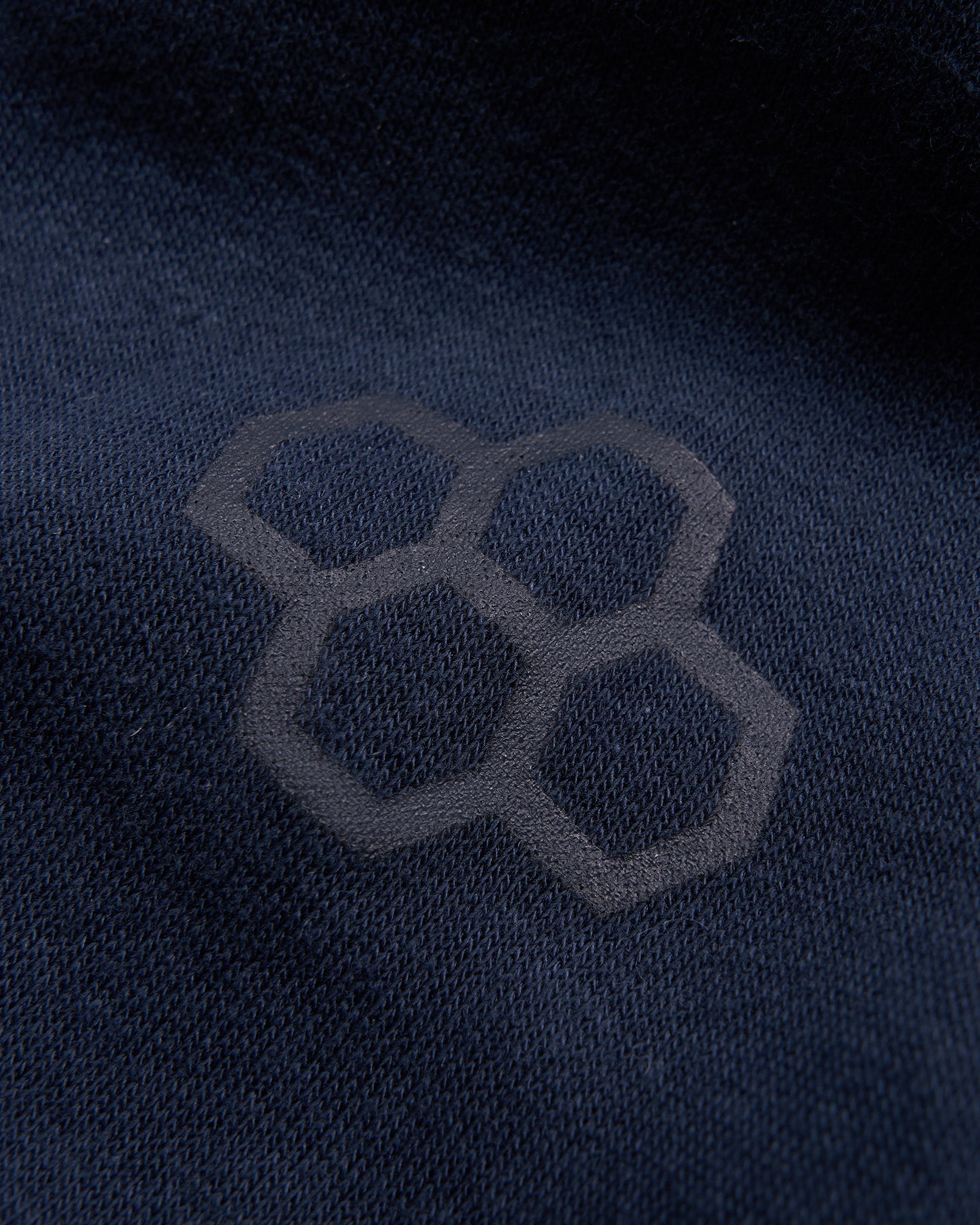 A close-up view of a navy fabric featuring a subtle hexagonal logo design emphasizing texture and branding