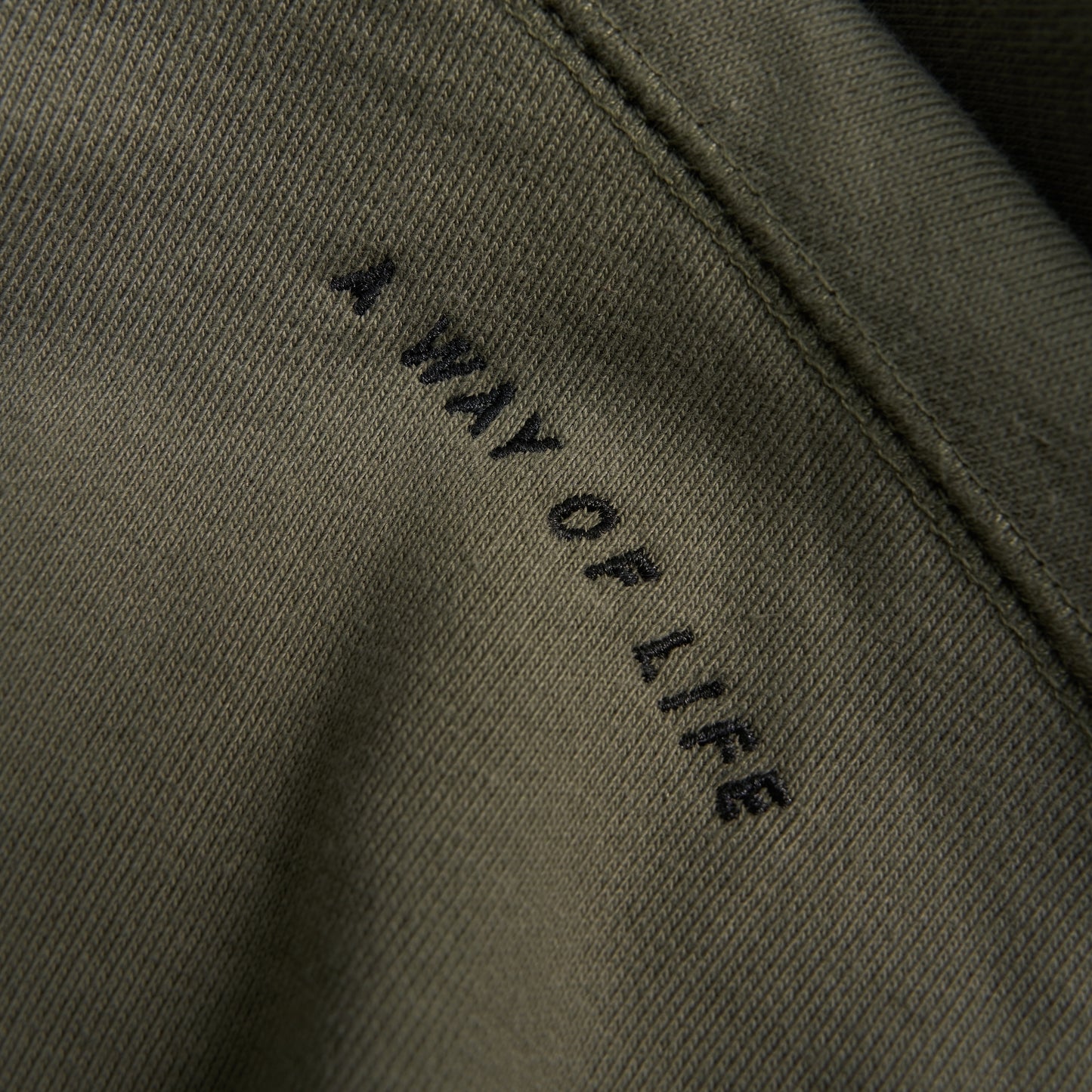 An olive green fabric featuring the embroidered phrase A WAY OF LIFE in black letters highlighting a minimalist style