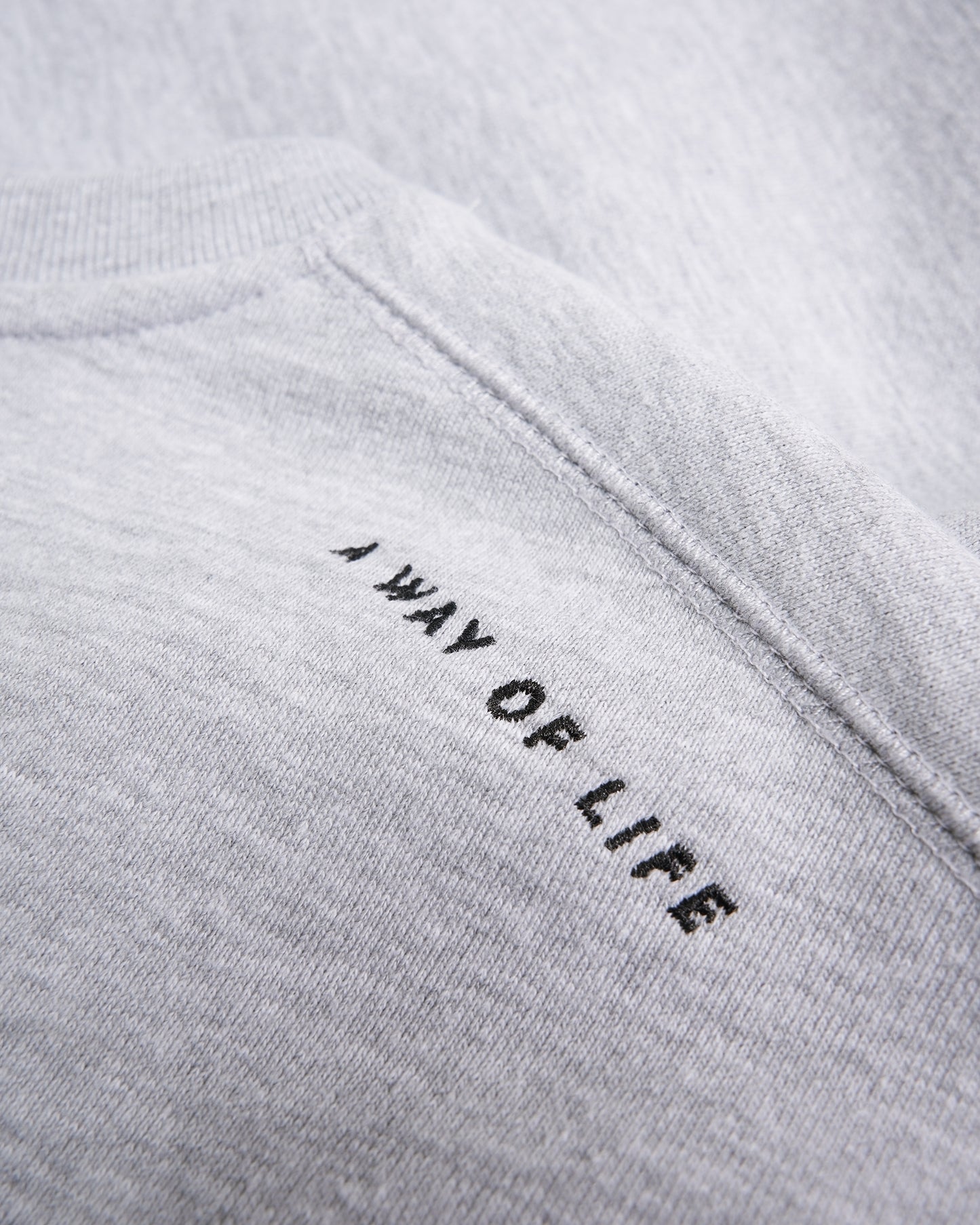 A close-up view of a light gray sweatshirt featuring the text A WAY OF LIFE embroidered in black on the upper back area