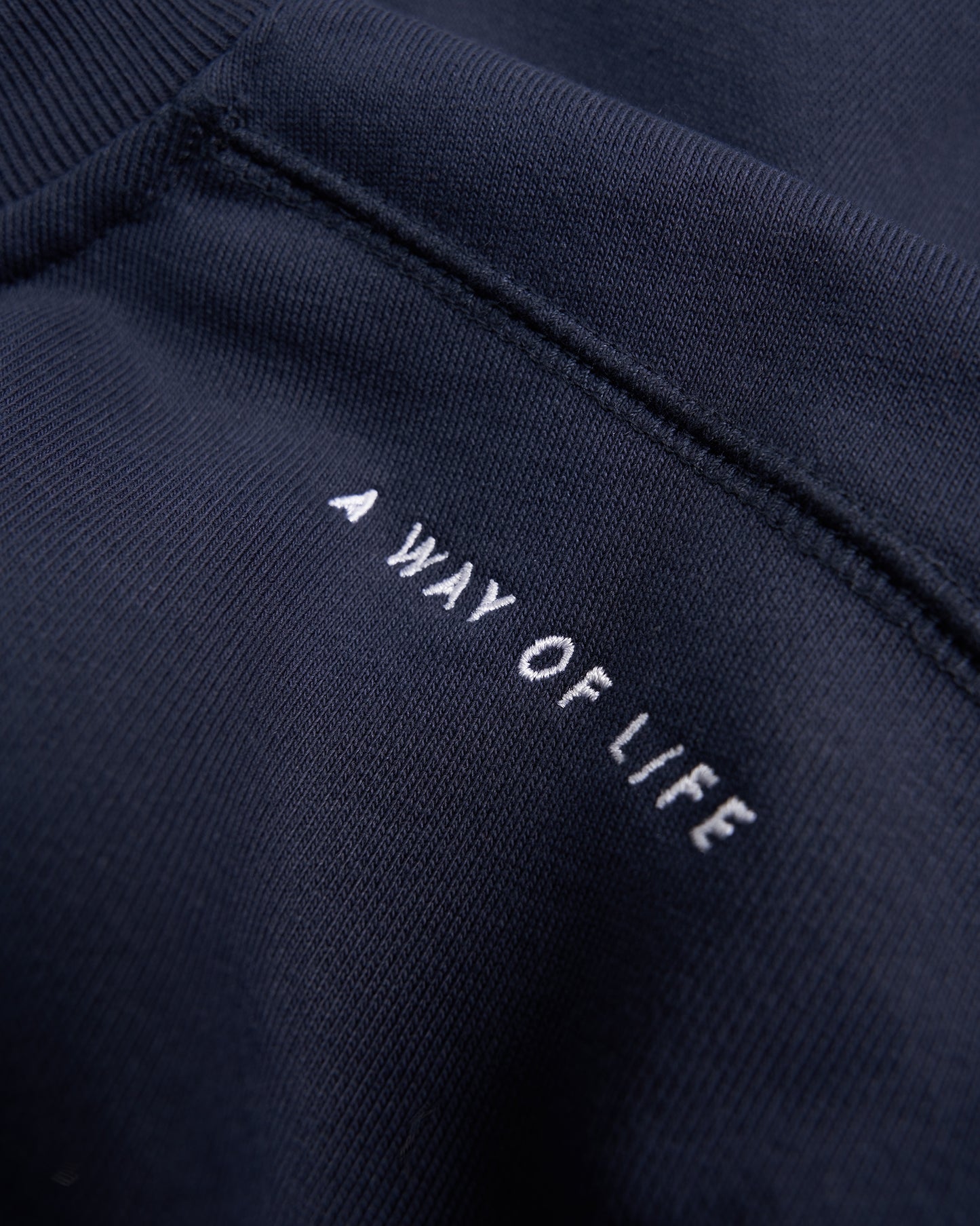 A close-up view of a dark navy garment featuring the phrase A WAY OF LIFE embroidered in white text