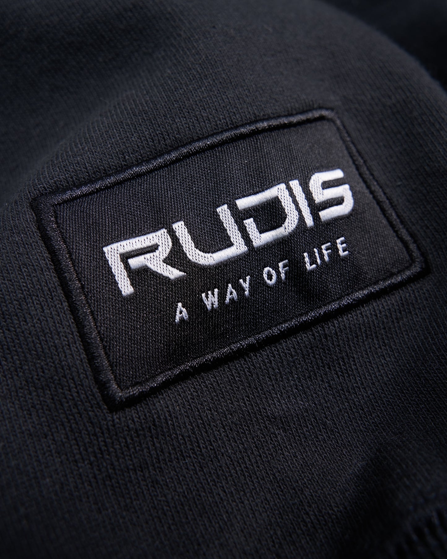 A close-up of the embroidered logo of RUDIS on a black garment featuring the phrase A WAY OF LIFE