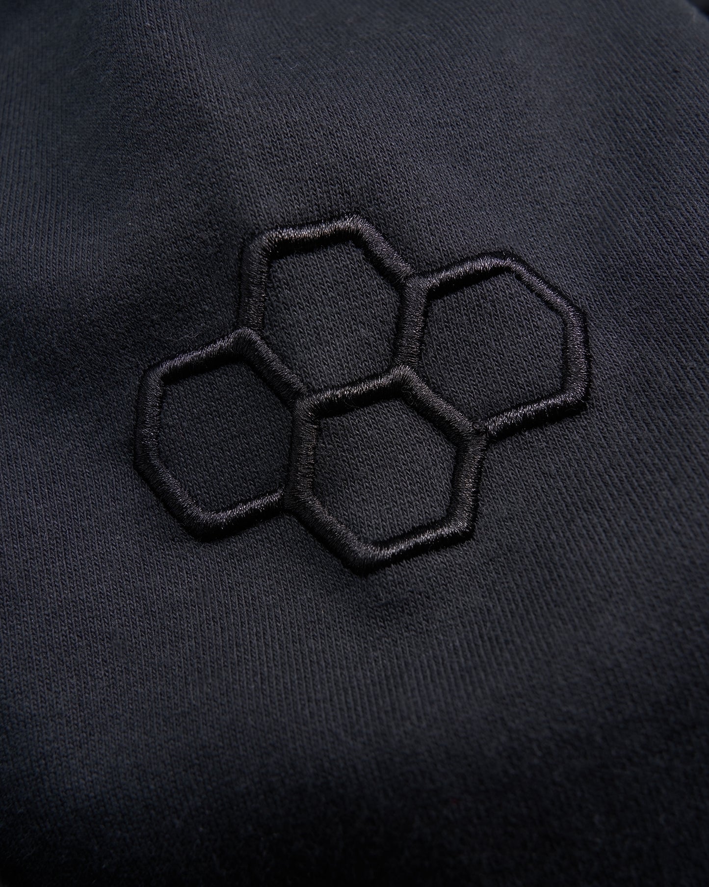 A close-up view of a black fabric featuring an embroidered hexagonal pattern emphasizing texture and design details