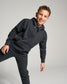 A cheerful young boy poses in a black hoodie and matching sweatpants demonstrating a playful and casual style against a neutral backdrop