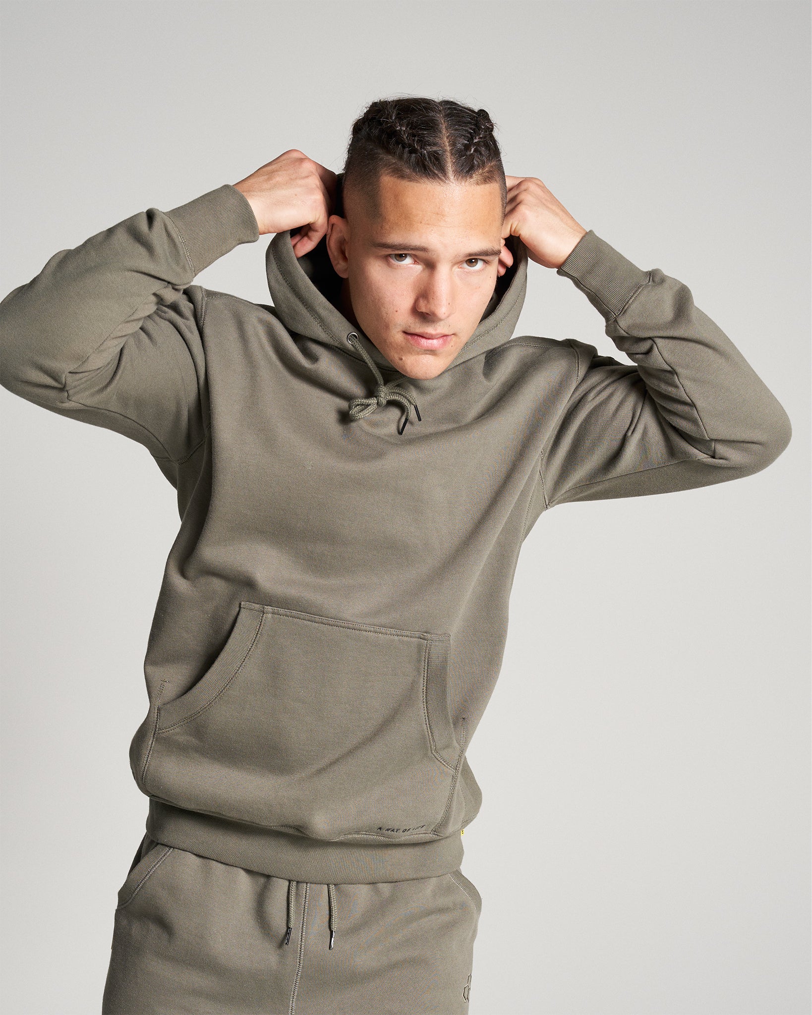 A young man adjusts the hood of his stylish olive green sweatshirt showcasing a contemporary and relaxed aesthetic