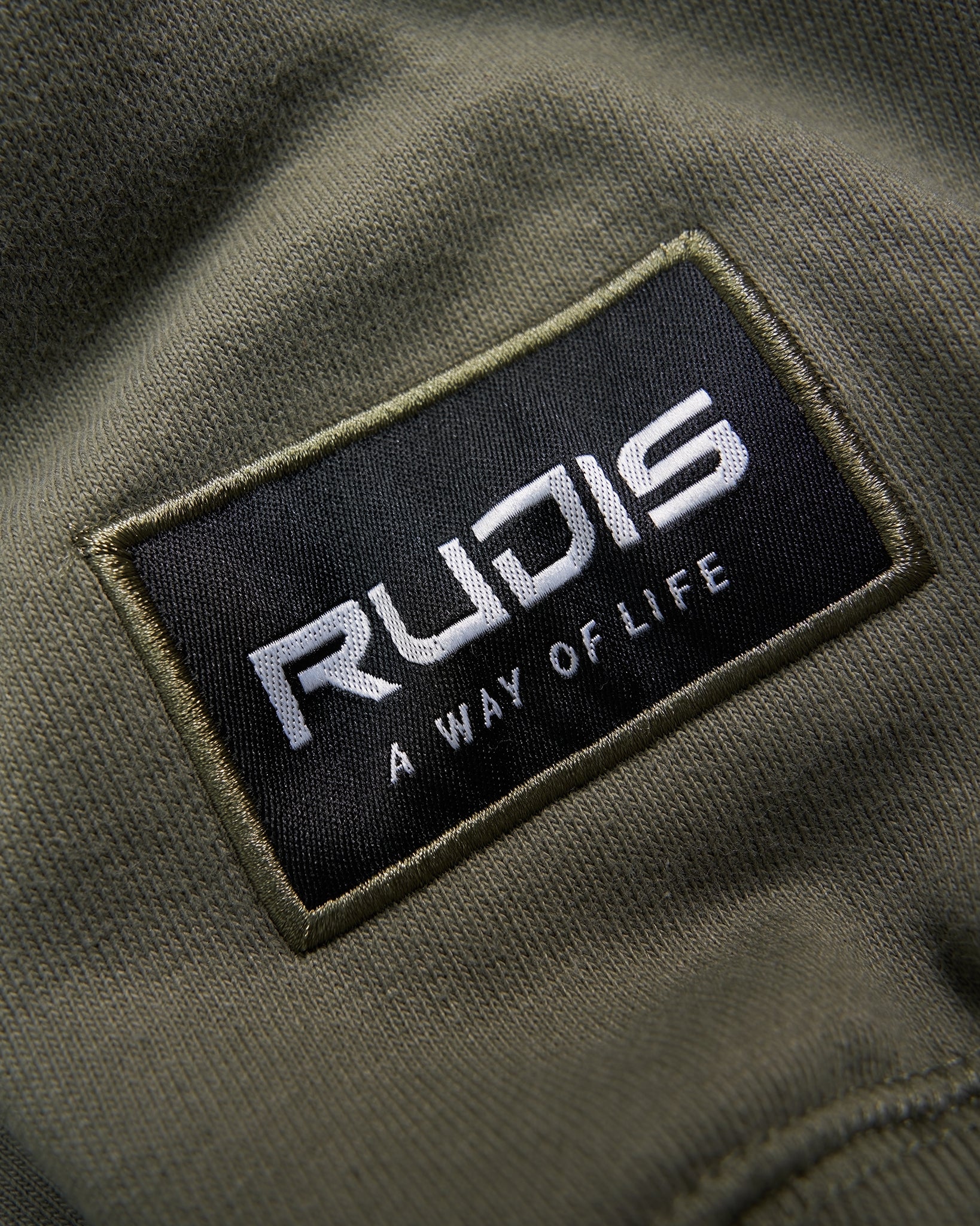 Embroidered patch from a clothing brand featuring the word RUDIS and the phrase A WAY OF LIFE on an olive green fabric background