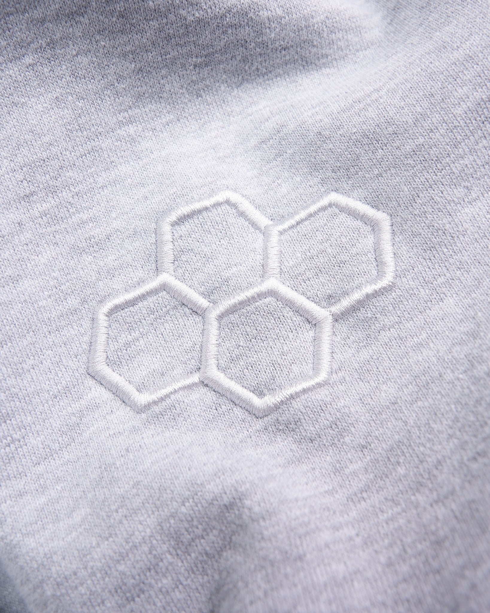 A close-up view of a light gray fabric featuring an embroidered hexagonal pattern in white