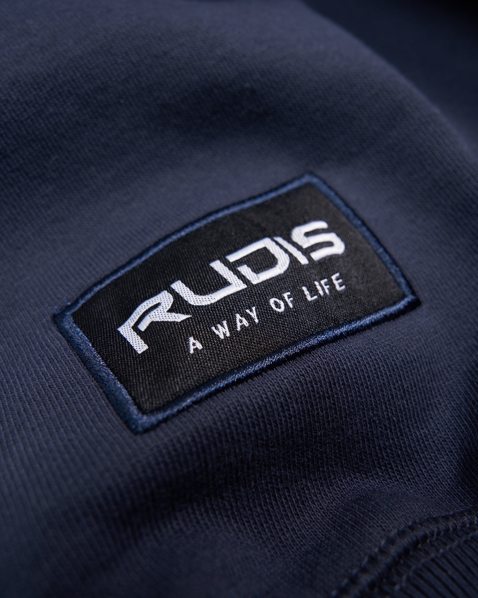 Close-up of a RUDIS brand logo on a navy fabric background that promotes a lifestyle centered around wrestling