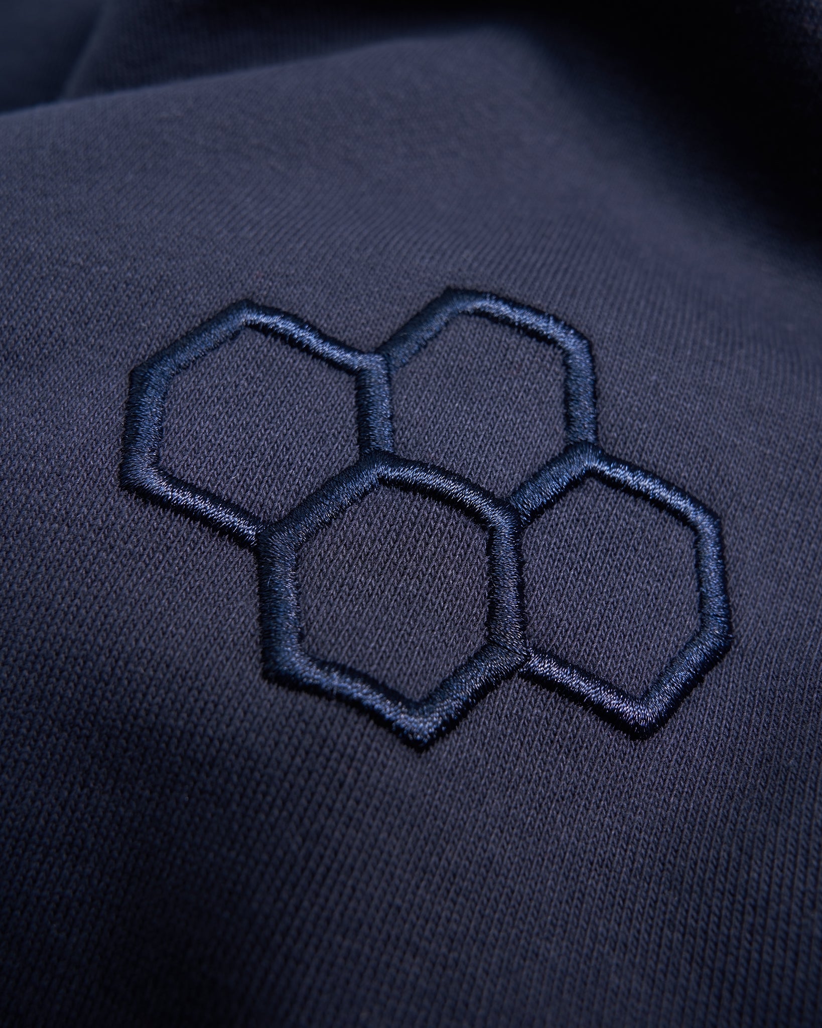 An embroidered design of interconnected hexagons in a dark navy fabric showcasing a clean and modern aesthetic