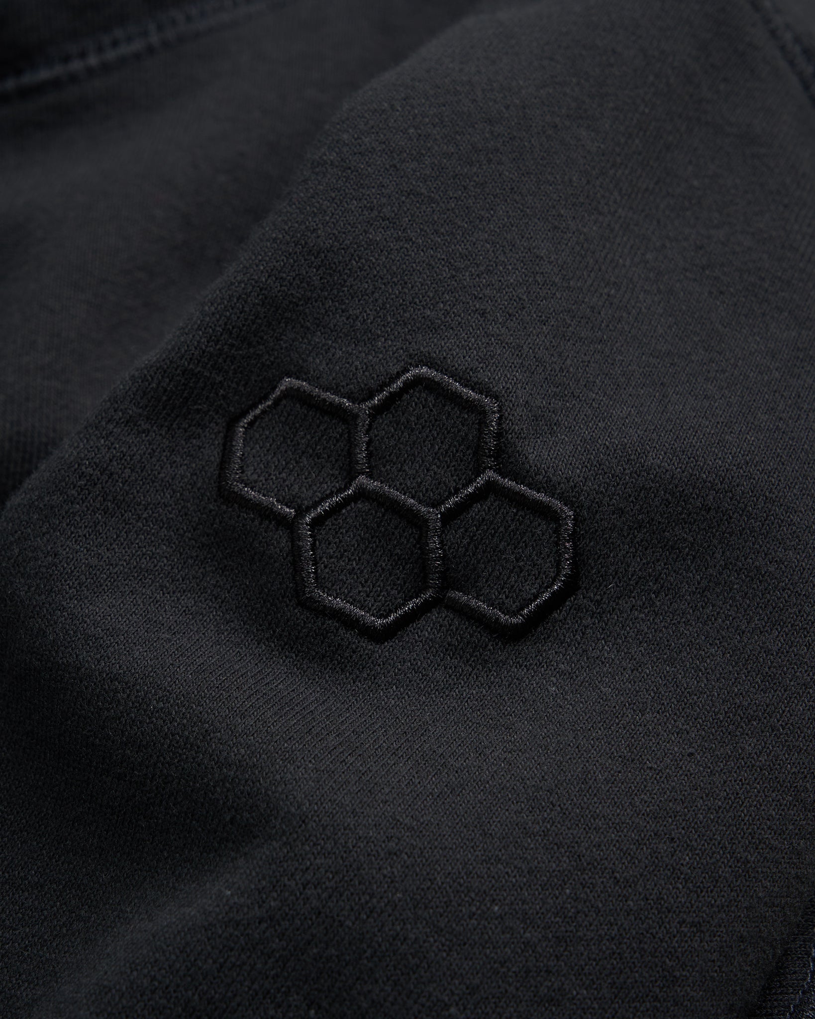 Close-up of a black fabric featuring an embroidered hexagonal logo in a subtle design