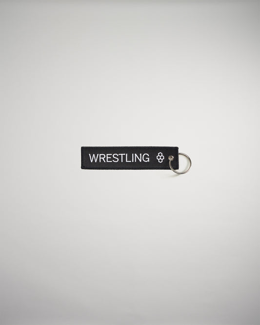 A black keychain tag featuring the word WRESTLING in bold white letters attached to a silver metal ring