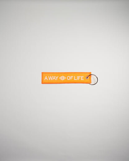 An orange fabric tag with the text A WAY OF LIFE displayed prominently attached to a metal keyring