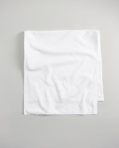 A soft white rectangular towel featuring a subtle hexagonal pattern in the corner resting on a neutral background