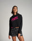 A young woman poses confidently in a black cropped hoodie featuring bold pink lettering and matching gray camo shorts highlighting a sporty aesthetic