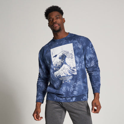 A man wearing a blue tie-dye sweatshirt featuring a wave graphic paired with gray athletic pants and evoking a casual trendy vibe