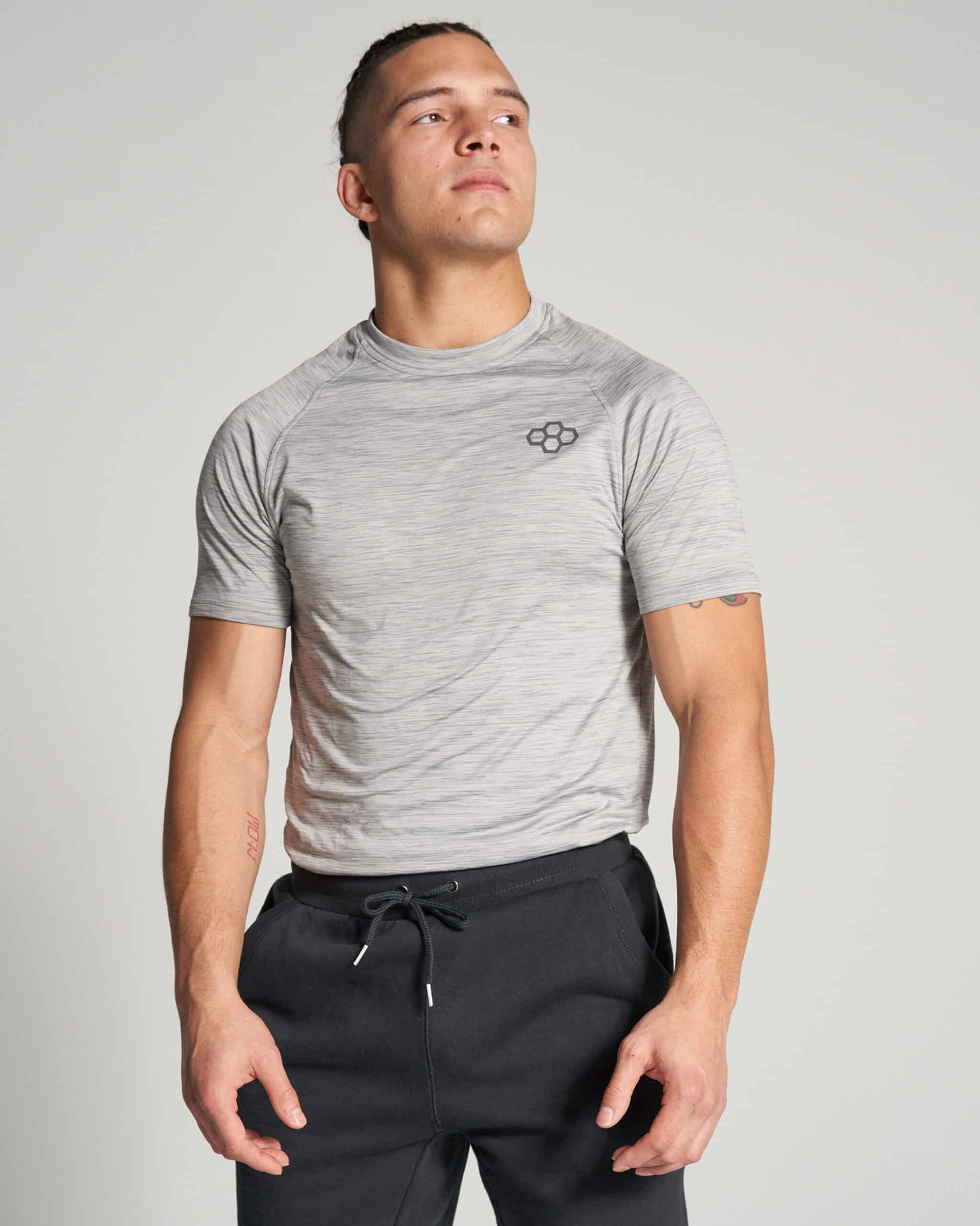 A young man poses confidently in a light gray athletic shirt and dark sweatpants showcasing a stylish and functional workout ensemble