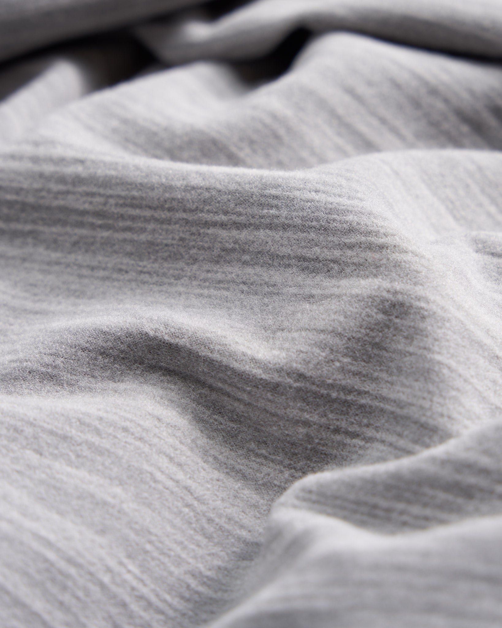 A close-up view of soft light gray fabric with a textured pattern showcasing intricate folds and waves that emphasize its softness and fluidity