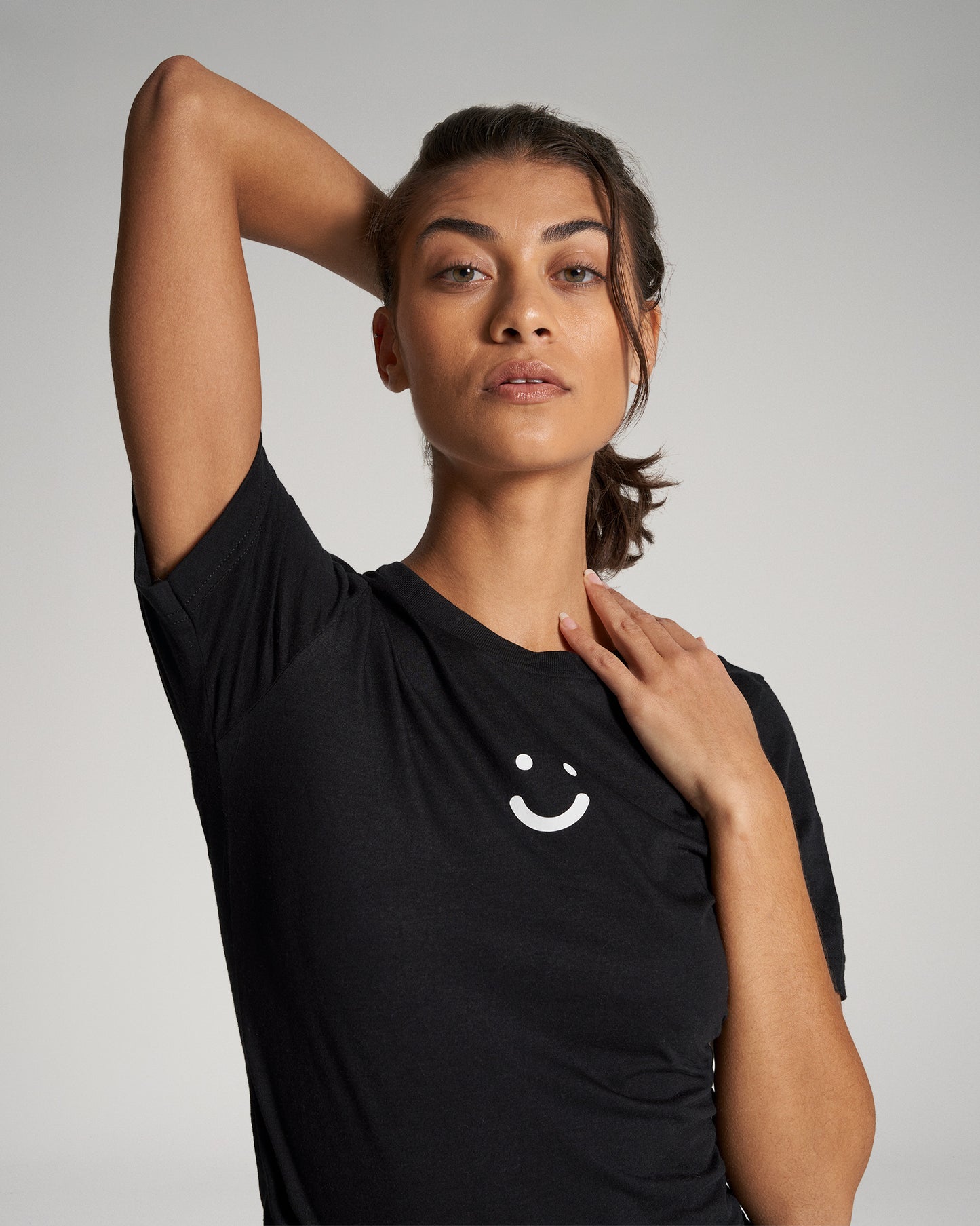 A woman poses confidently in a black t-shirt with a minimalistic smiley face design showcasing her natural beauty and relaxed demeanor