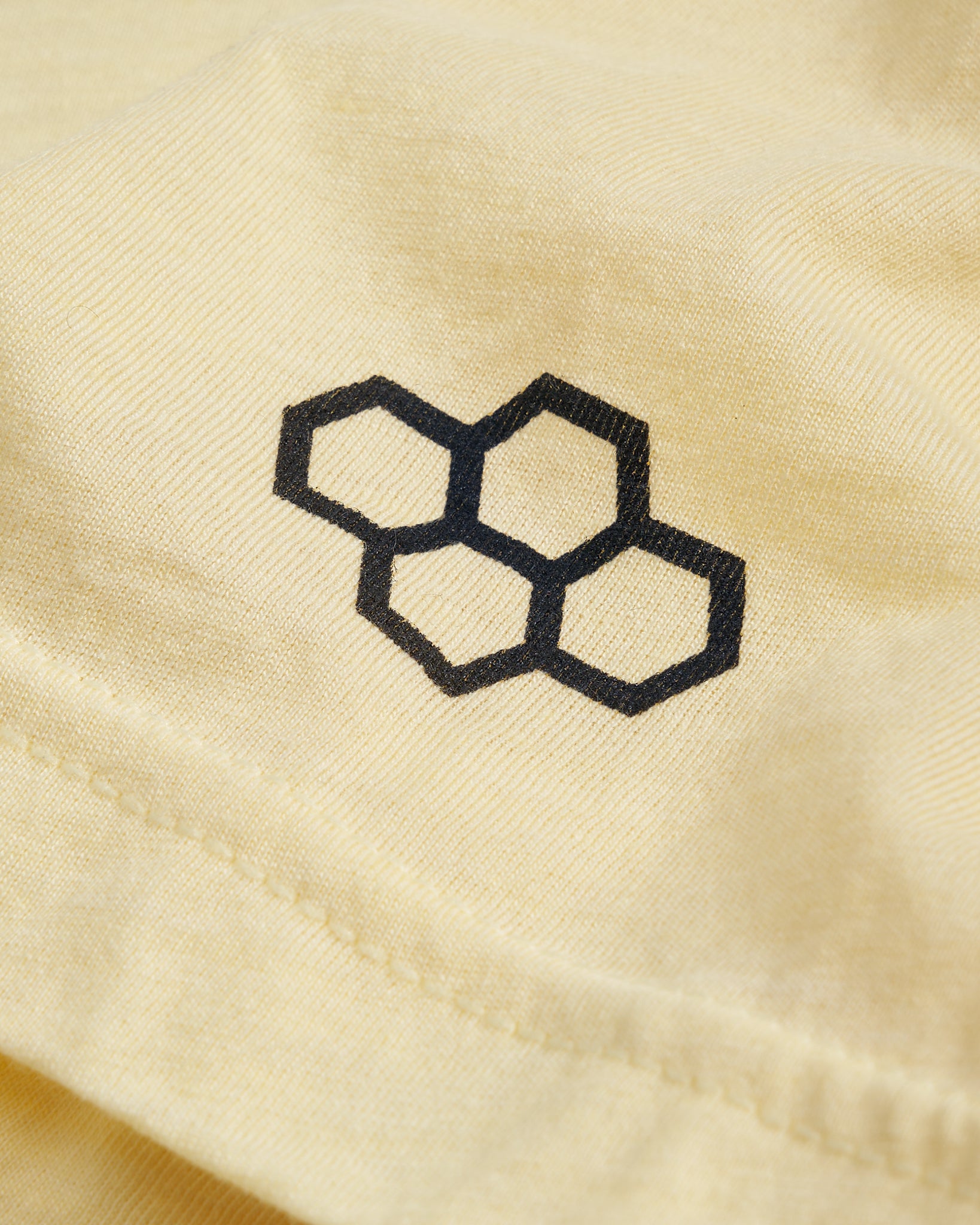 A close-up view of a yellow fabric featuring a black honeycomb logo capturing the texture and stitching details of the material