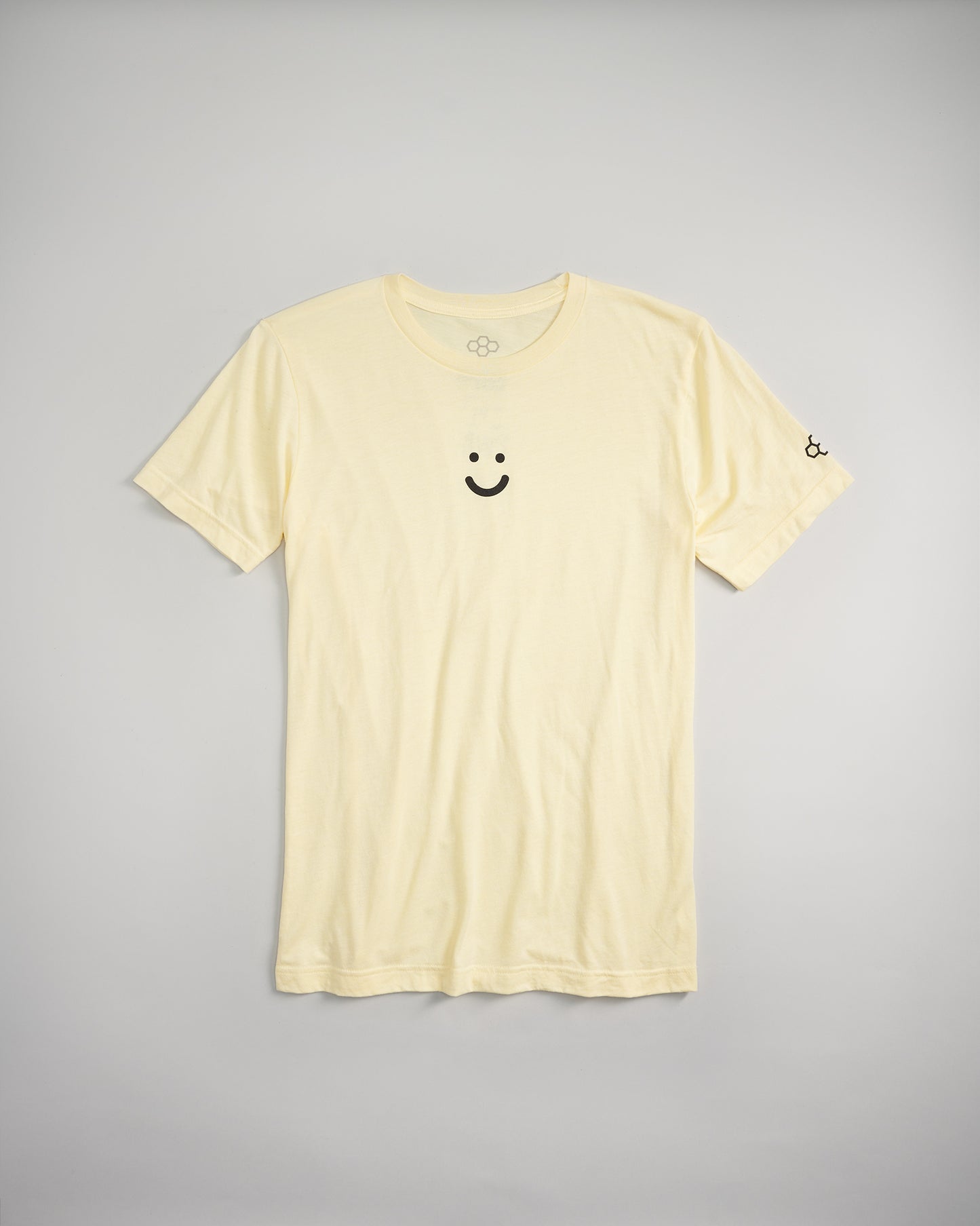 A light yellow t-shirt featuring a black smiley face design on the front and a small logo on the sleeve