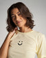 A woman with wavy hair is smiling wearing a pale yellow t-shirt featuring a simple black smiley face design on the front