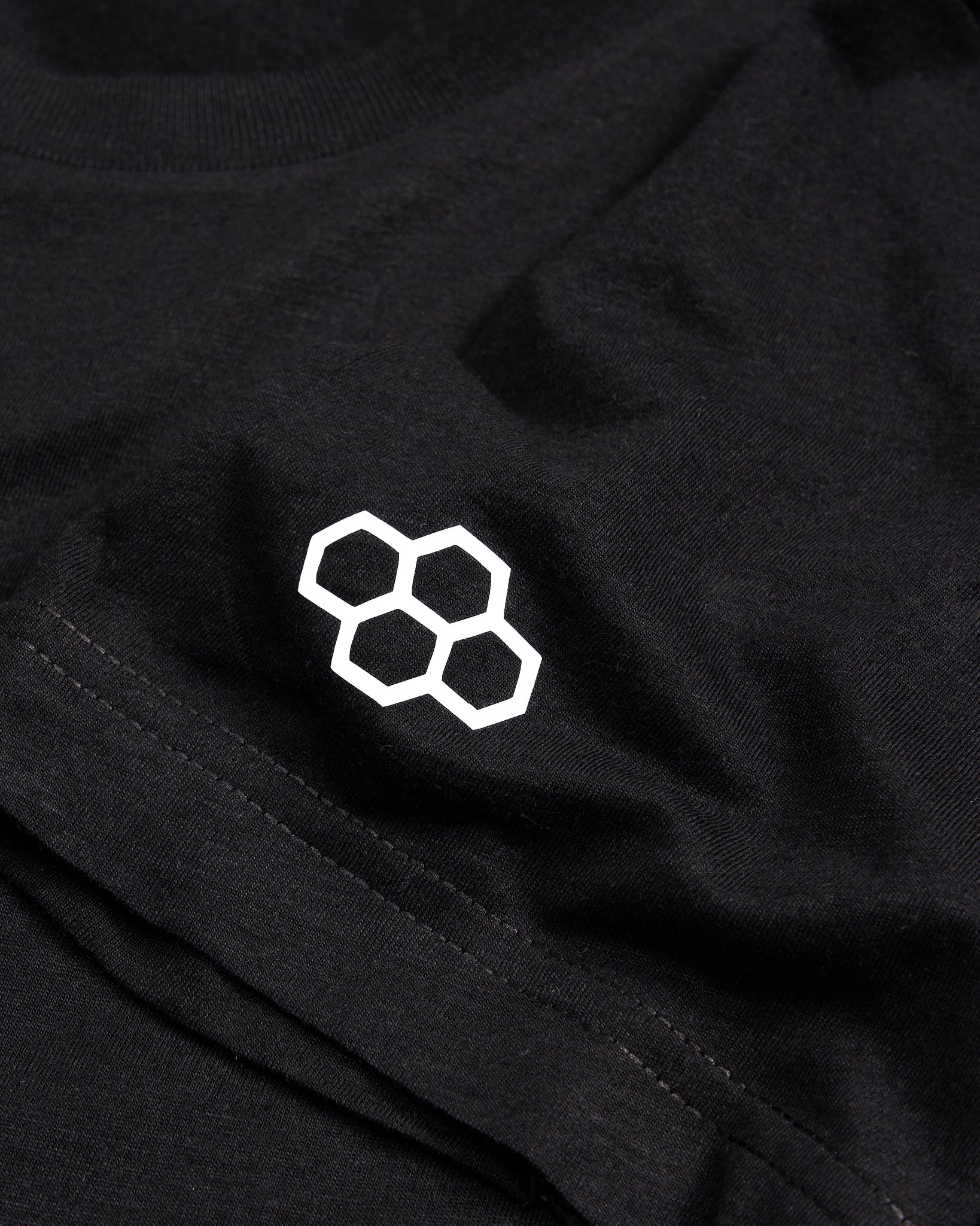 A close-up view of a black t-shirt featuring a minimalist white honeycomb logo on the chest area