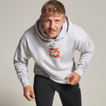 A man confidently poses in a light gray hoodie with a colorful graphic design on the front paired with black sweatpants in a neutral background setting