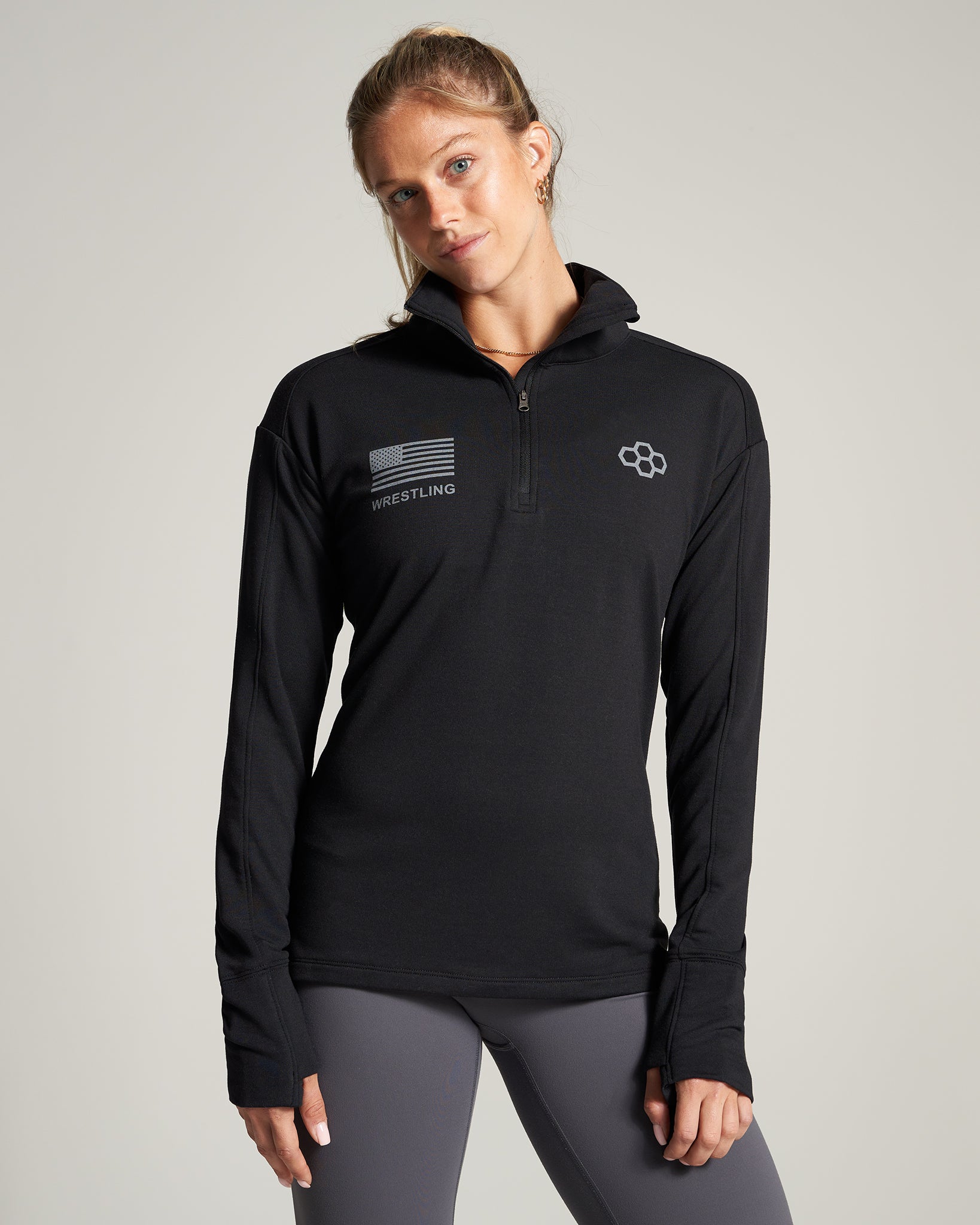 A female athlete models a black long-sleeve pullover with a zippered collar and wrestling-themed graphics