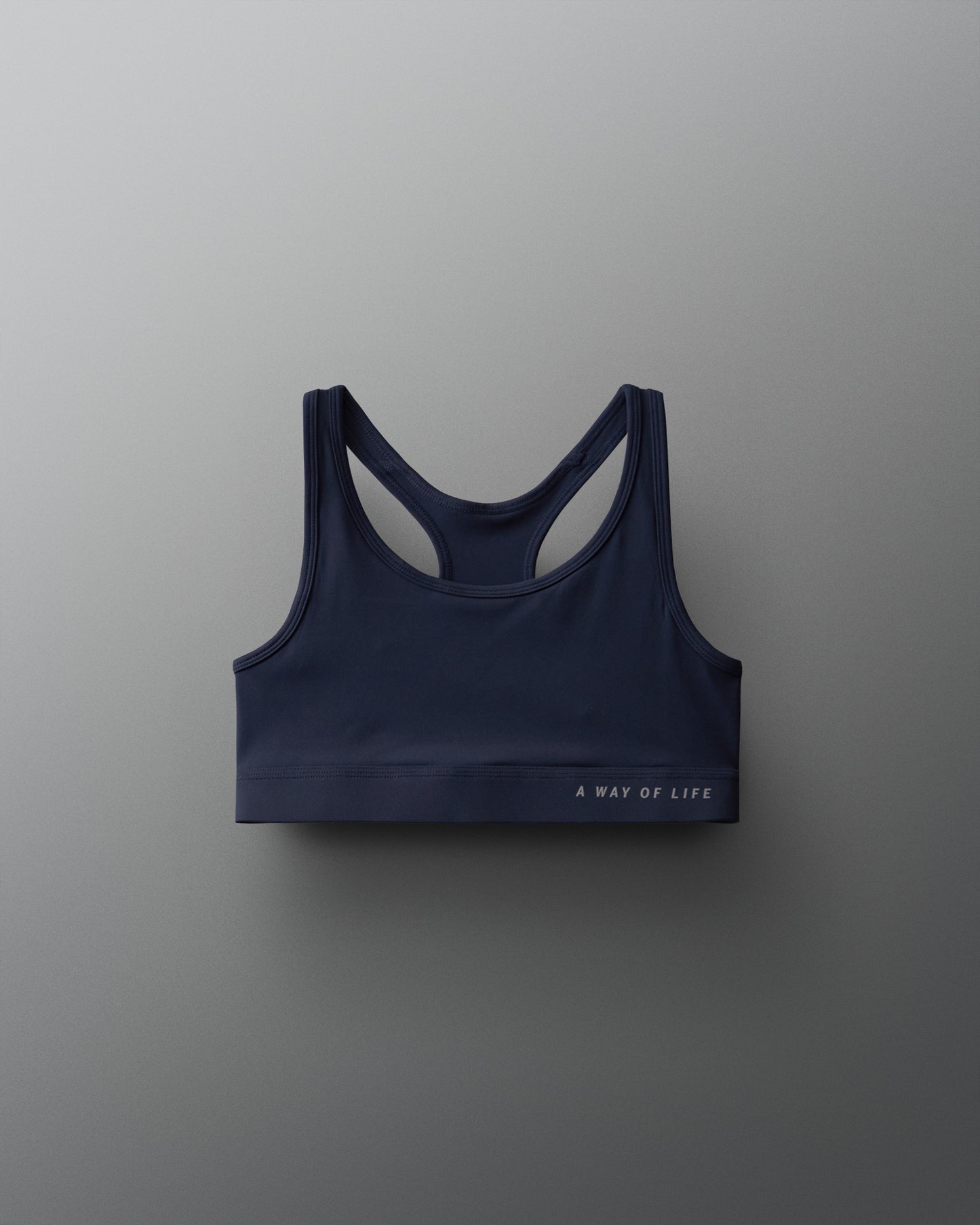 A navy blue sports bra with a racerback design on a gray background features the phrase 'A WAY OF LIFE' printed on the band, combining style and functionality for active wear.