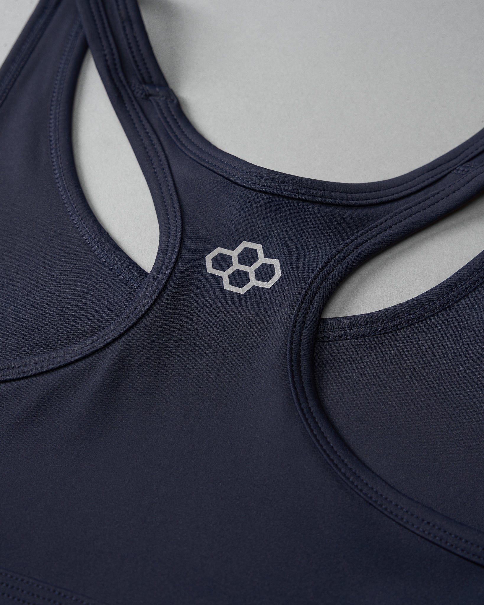 A close-up of a dark blue sports bra with multiple straps and a light-colored logo, emphasizing both style and functionality, set against a subtle gray background.