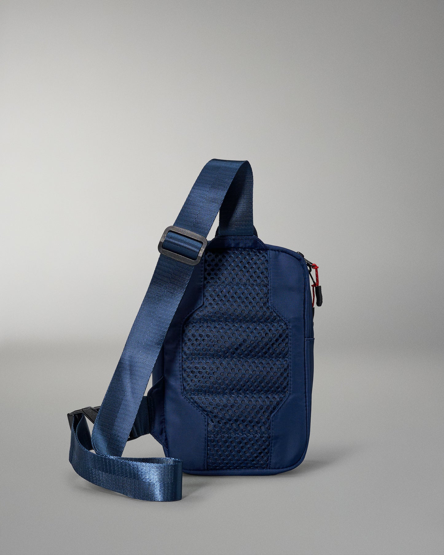 A navy crossbody bag with a textured back panel and an adjustable strap, designed for everyday use, stands against a soft gray background.