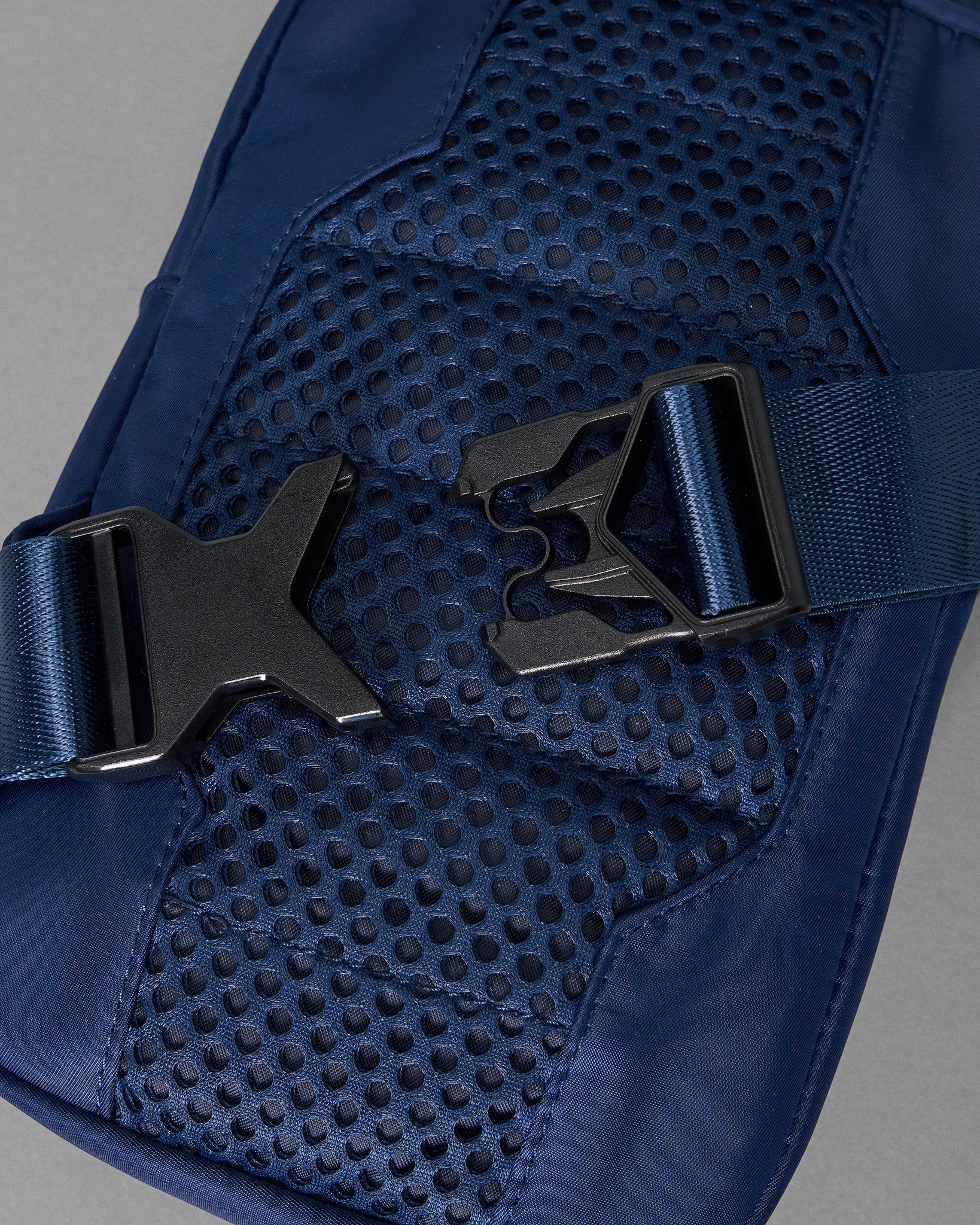 Close-up of a navy blue fabric with a breathable mesh area and a black buckle clasp, emphasizing functional design against a soft gray background.