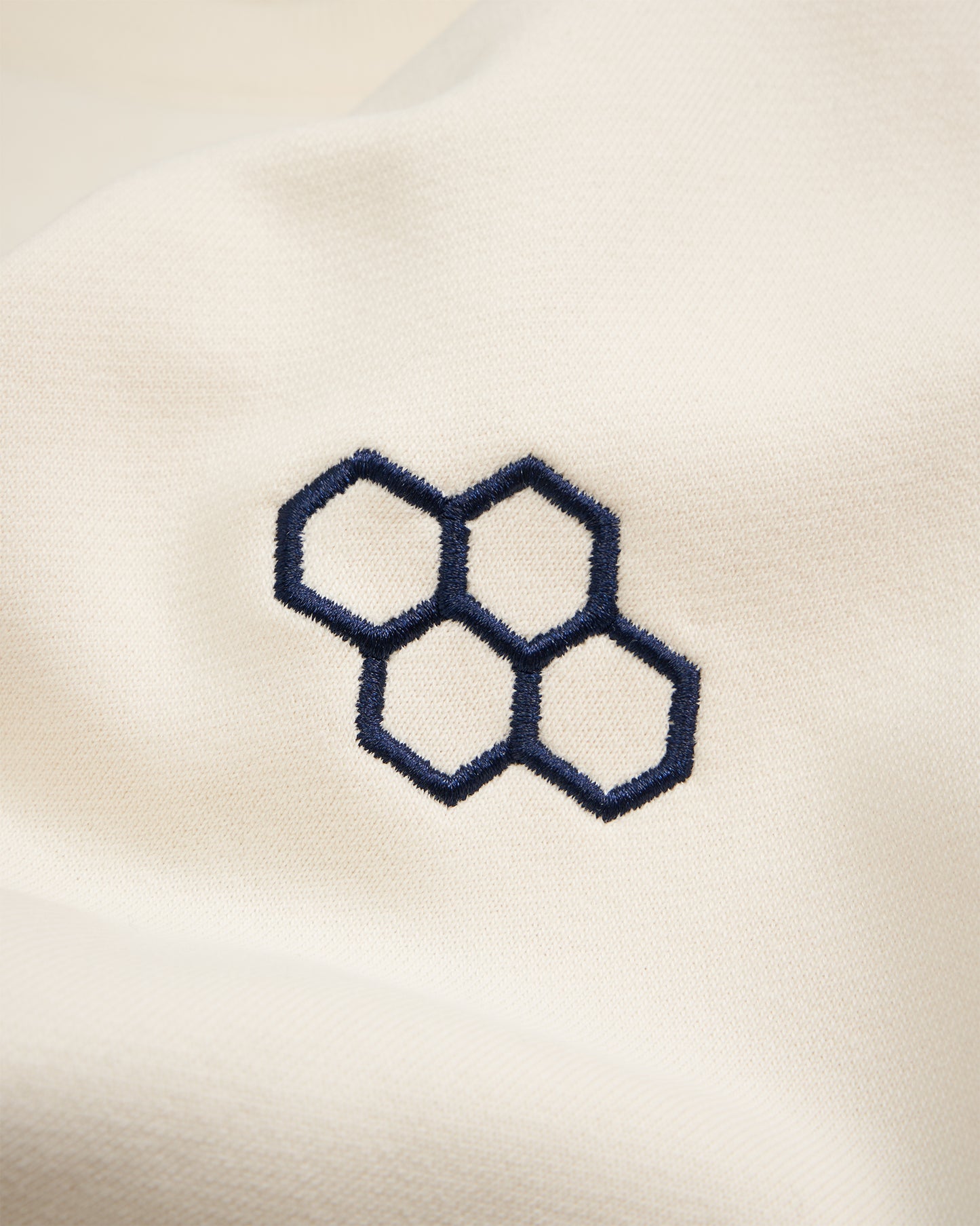 A close-up of a cream-colored fabric featuring an embroidered navy blue hexagon design