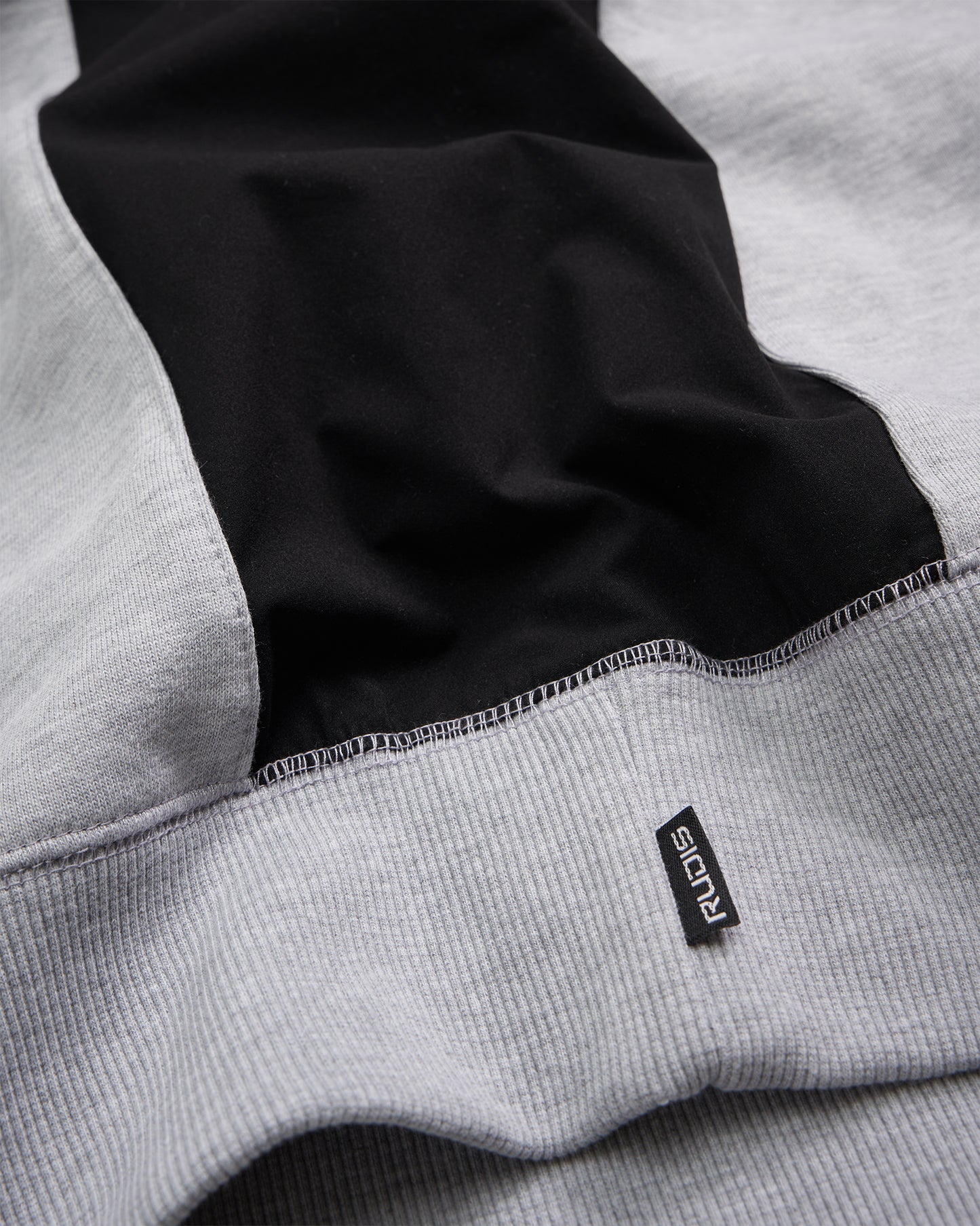 A close-up view of a stylish athletic sweater featuring a mix of gray and black fabric highlighting its textured weave and a fabric label