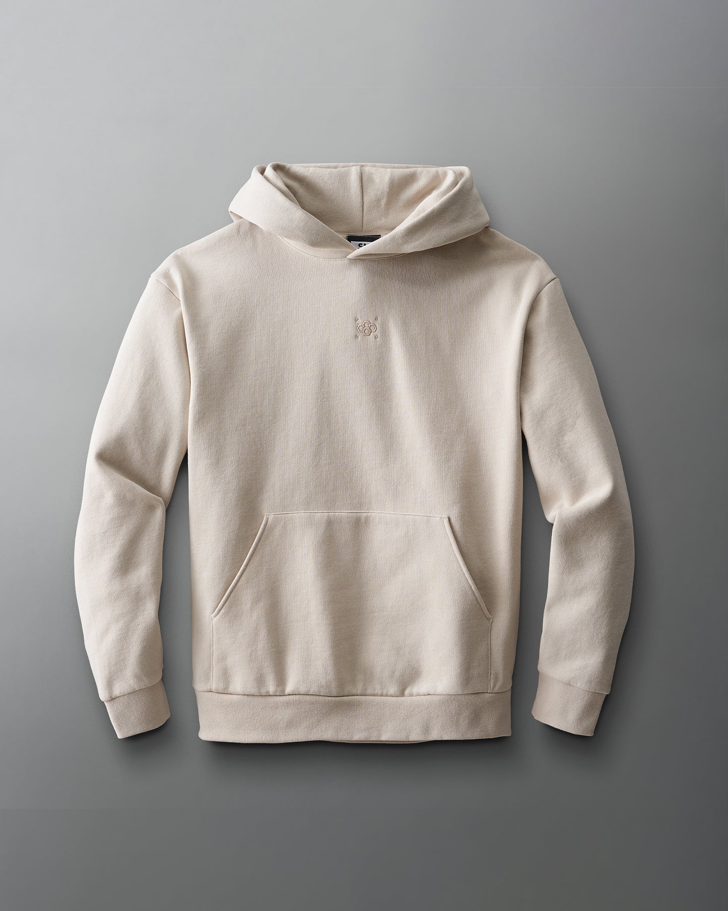 A light beige hoodie with a kangaroo pocket and an embroidered logo on the chest is showcased against a smooth gray background.