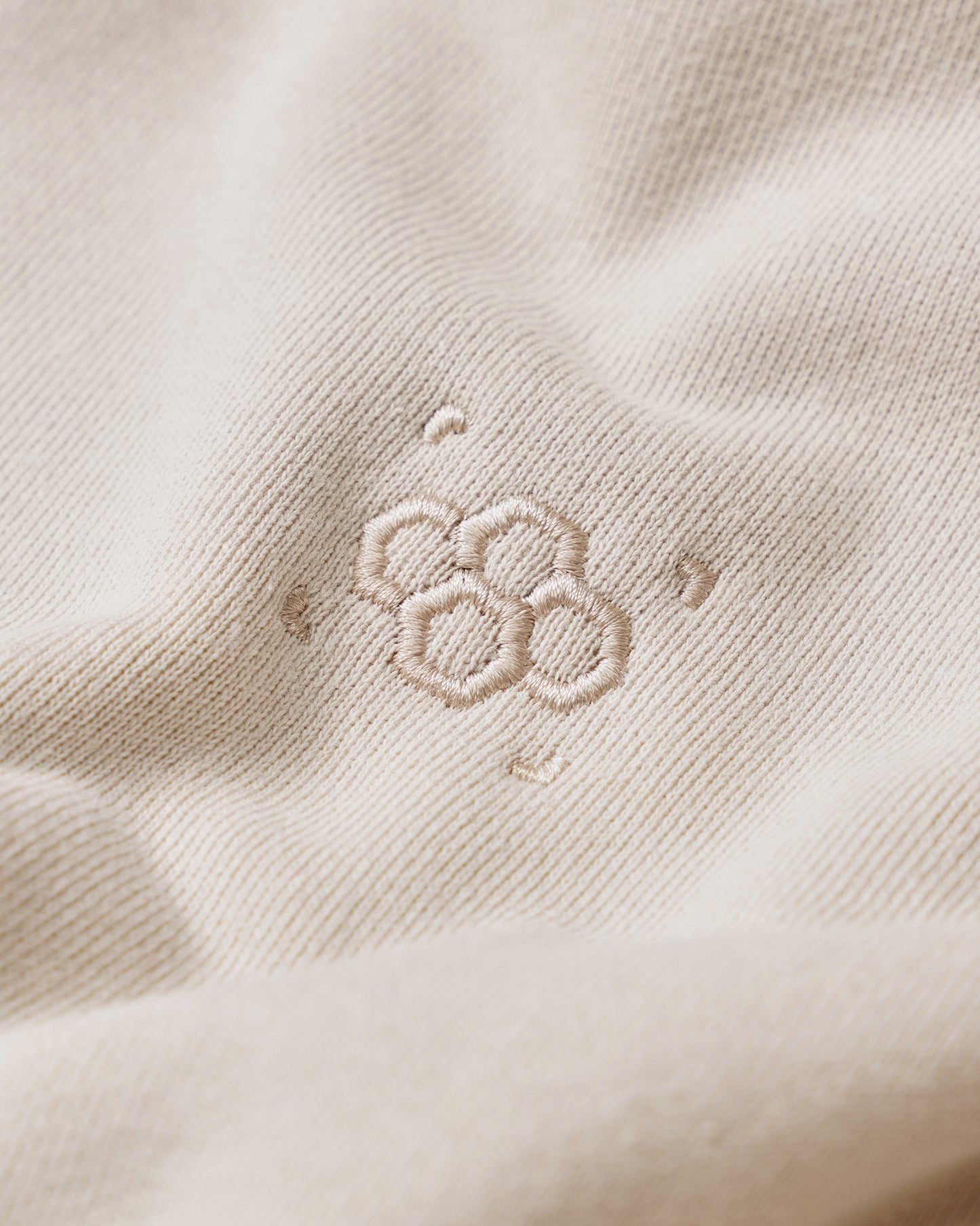 Close-up of a soft beige fabric with a delicate embroidered pattern of interconnected circles, showcasing a minimalist design that enhances its elegance.